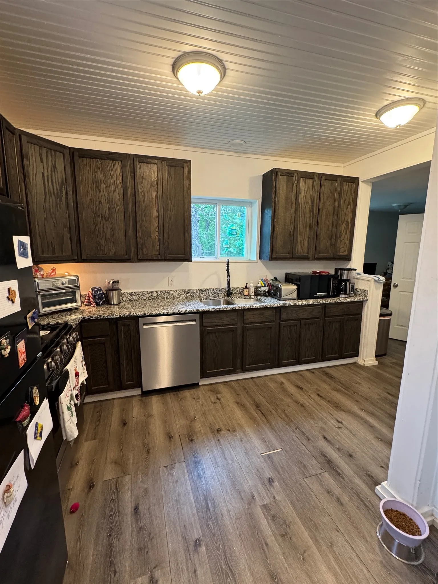 Kitchen with dark wood finish cabinetry, dark wood-style floors, stainless steel dishwasher, gas stove, and light stone counters