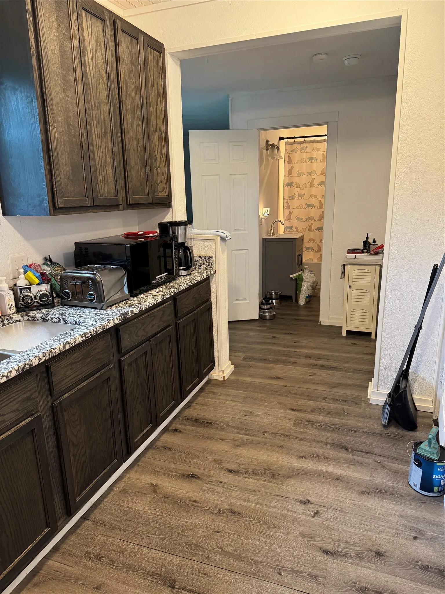 Kitchen with dark wood finish cabinets, dark wood finished floors, black microwave, and light stone counters