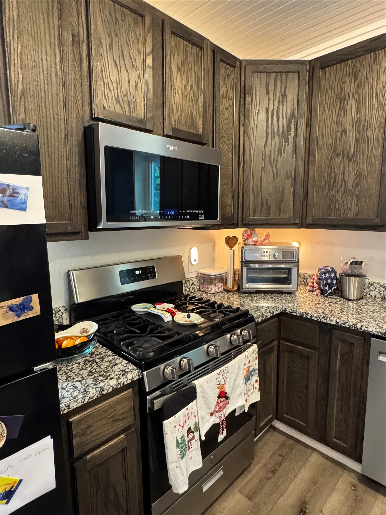 Kitchen featuring stainless steel appliances, dark wood finish cabinetry, light wood-style flooring, and light stone countertops