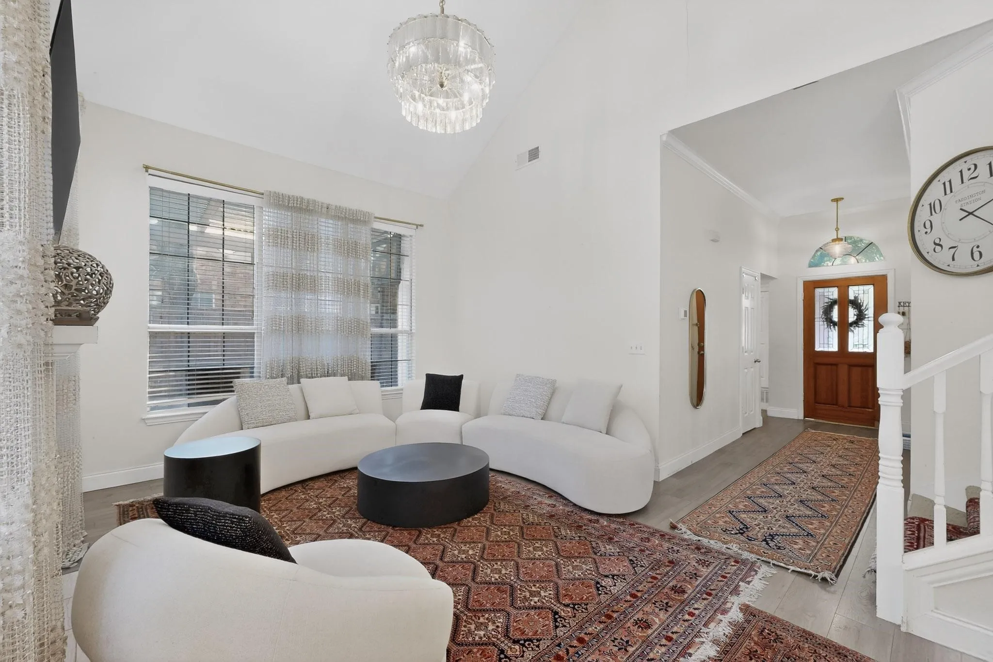 This living space features high vaulted ceilings, large windows with blinds, and light-colored flooring
