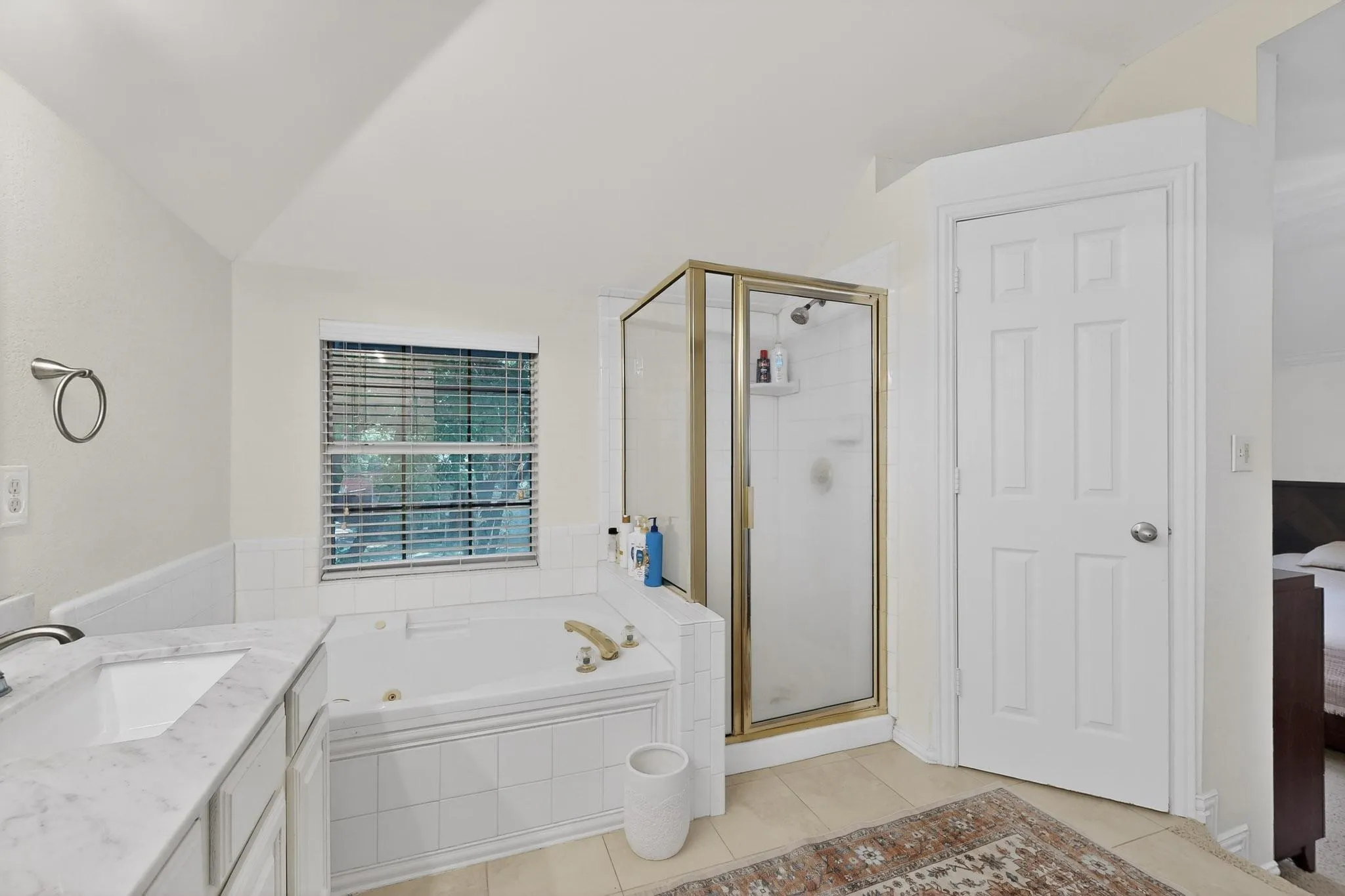 Ensuite bathroom with vanity, a shower stall, vaulted ceiling, a bath, and light tile patterned floors