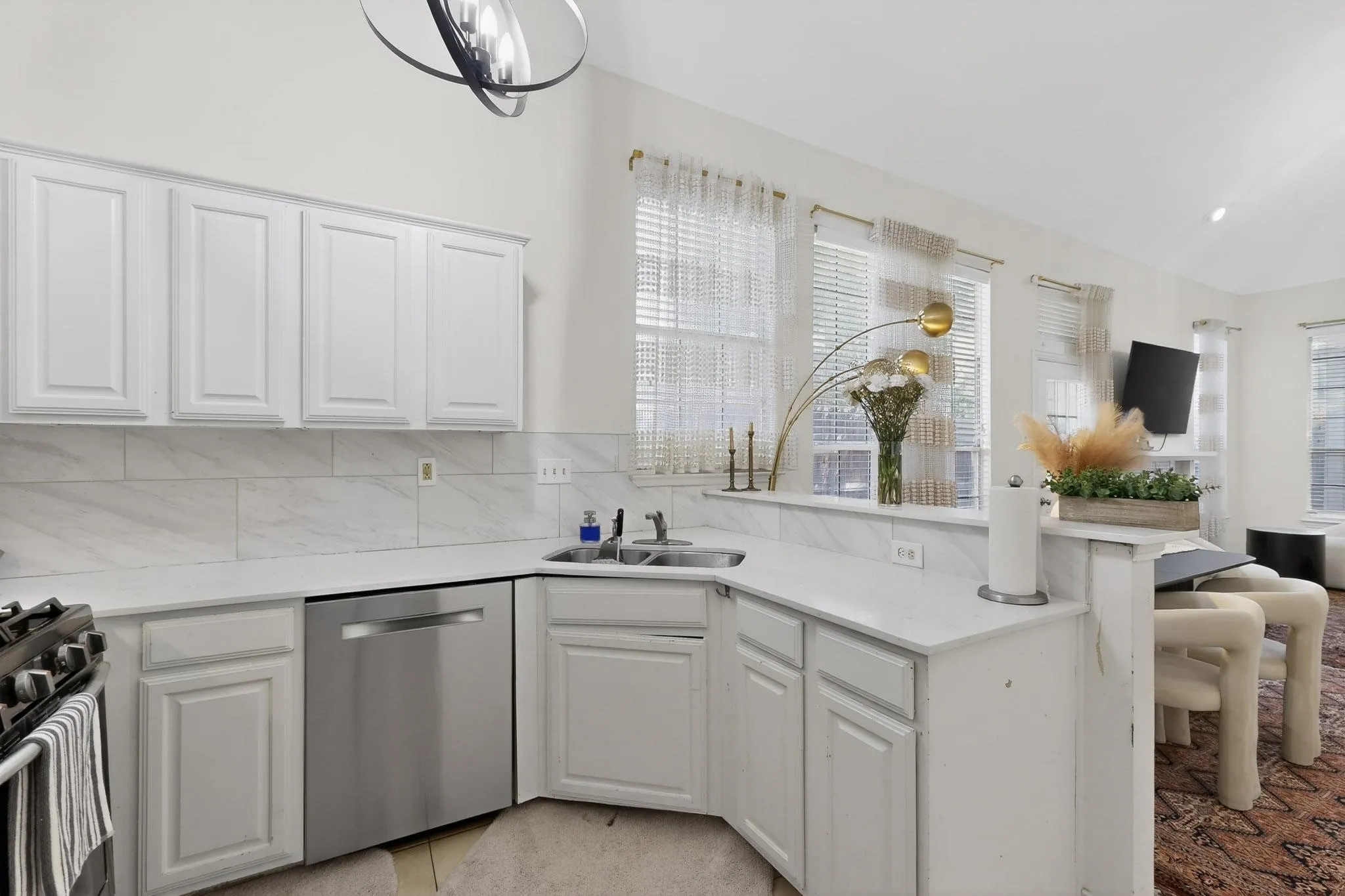 The kitchen features white cabinetry, light-colored countertops, a stainless steel dishwasher, and an integrated sink