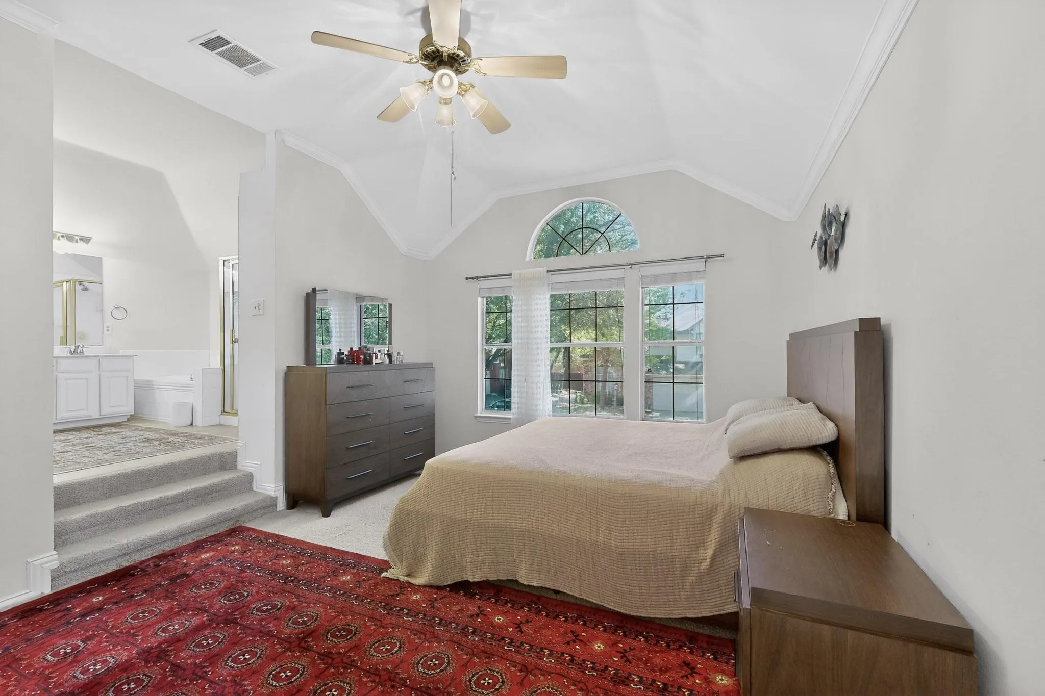 Bedroom with light carpet, ornamental molding, vaulted ceiling, ceiling fan, and connected bathroom