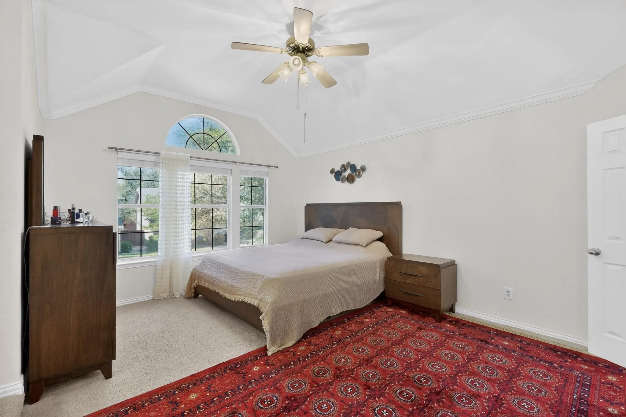 Bedroom with light colored carpet, vaulted ceiling, a ceiling fan, and ornamental molding