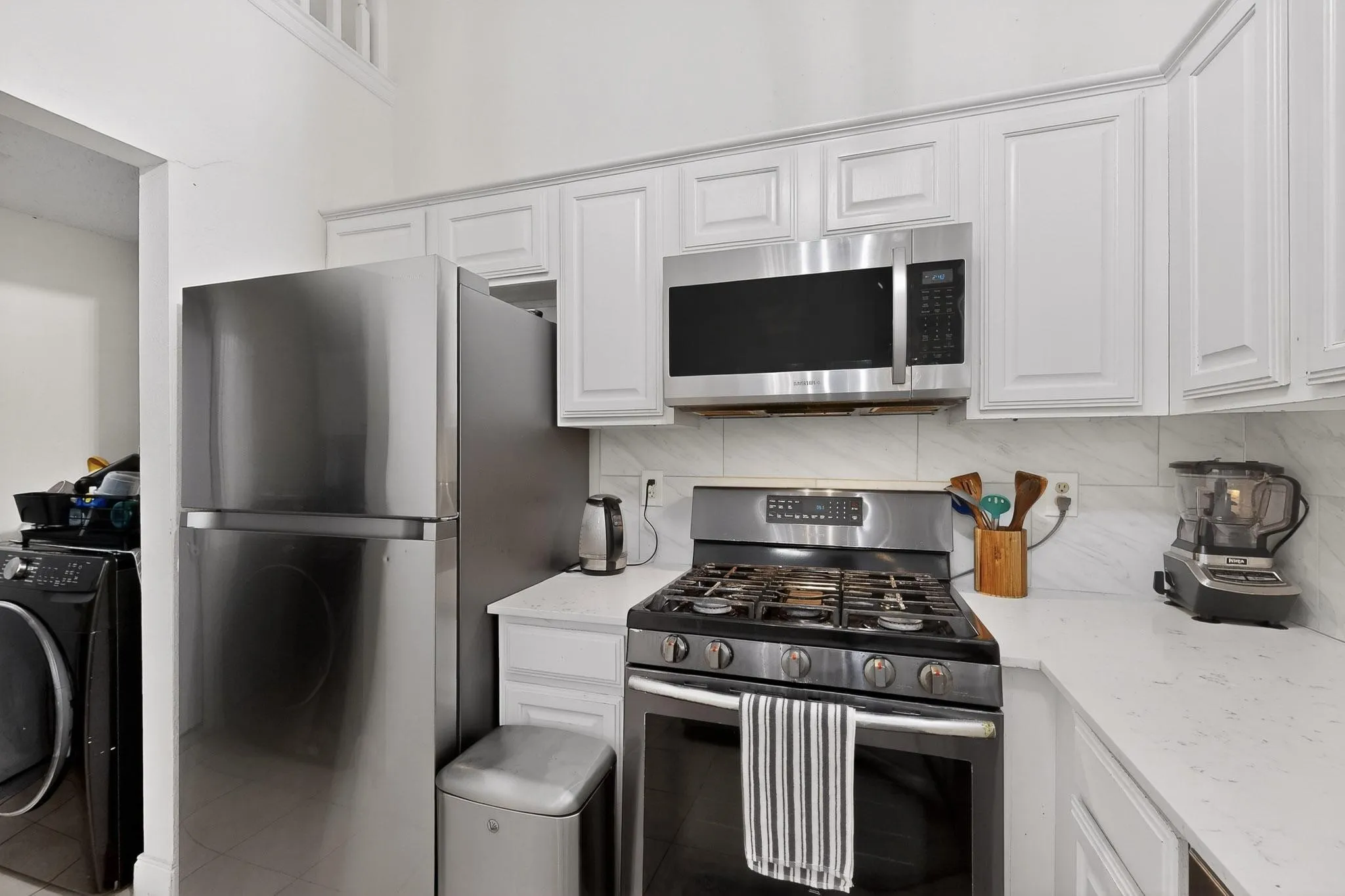 Kitchen featuring stainless steel appliances, washer / clothes dryer, white cabinets, light stone countertops, and decorative backsplash