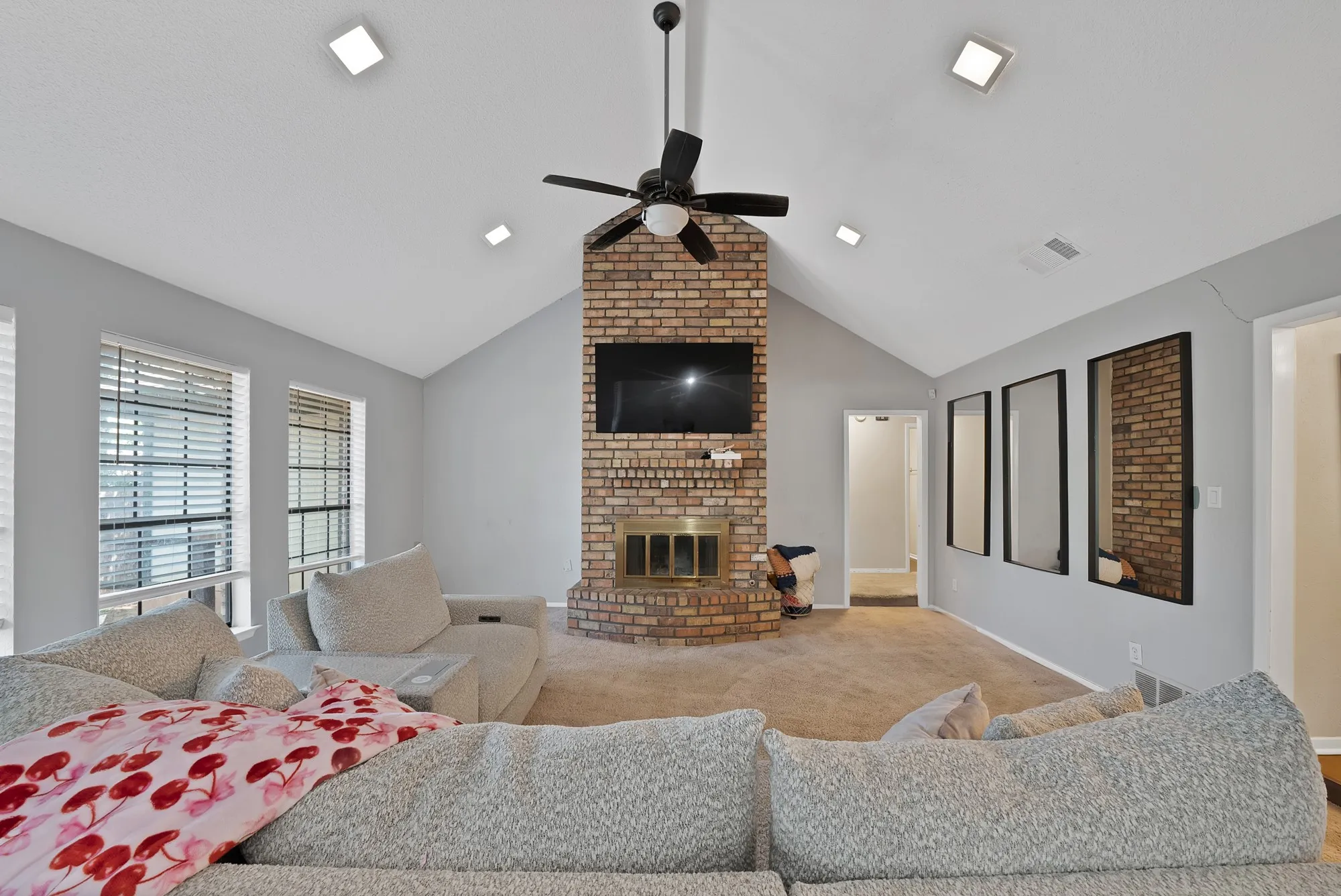 Carpeted living area with a ceiling fan and a brick fireplace