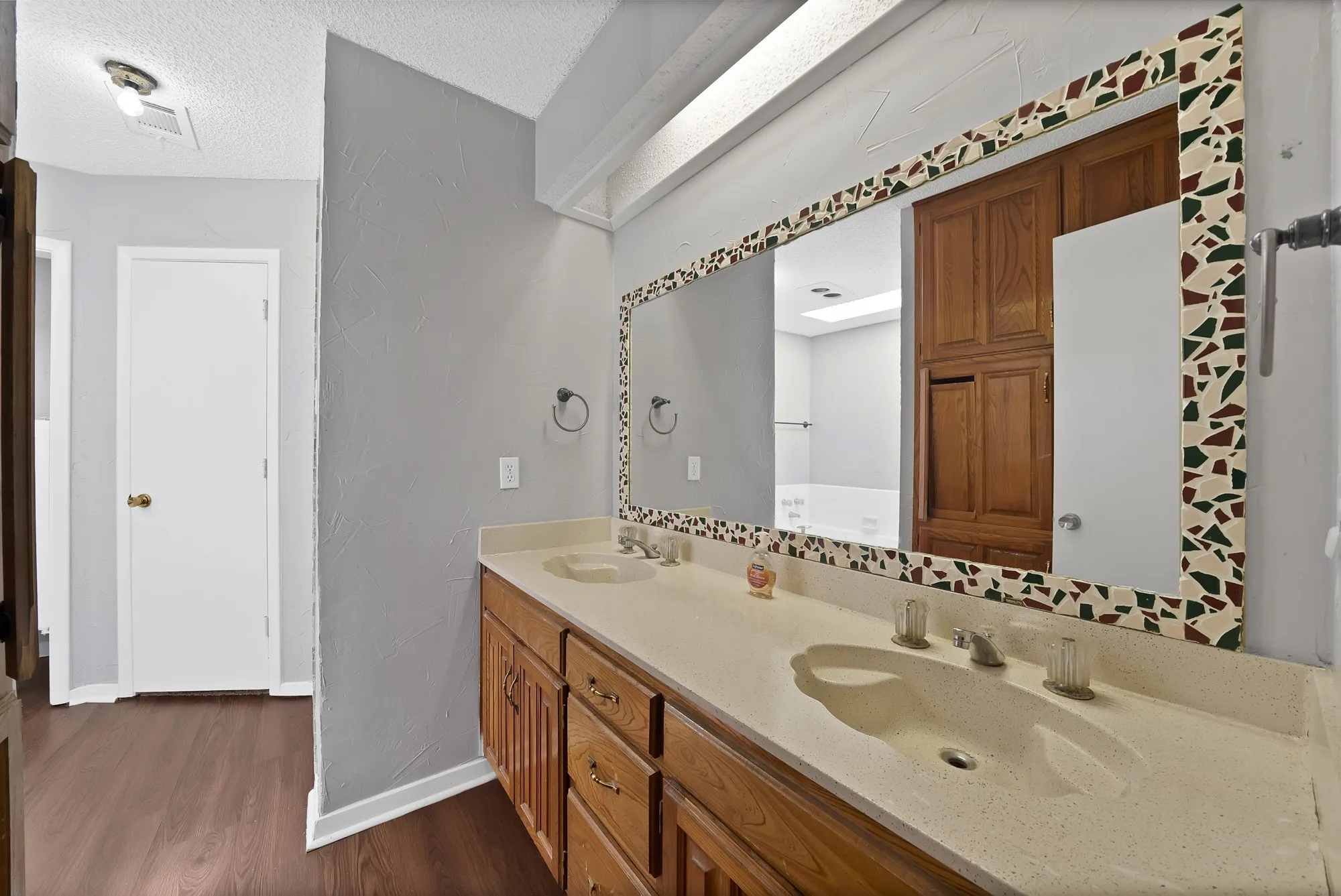 Full bath featuring double vanity, dark wood finished floors, a textured ceiling, and a textured wall