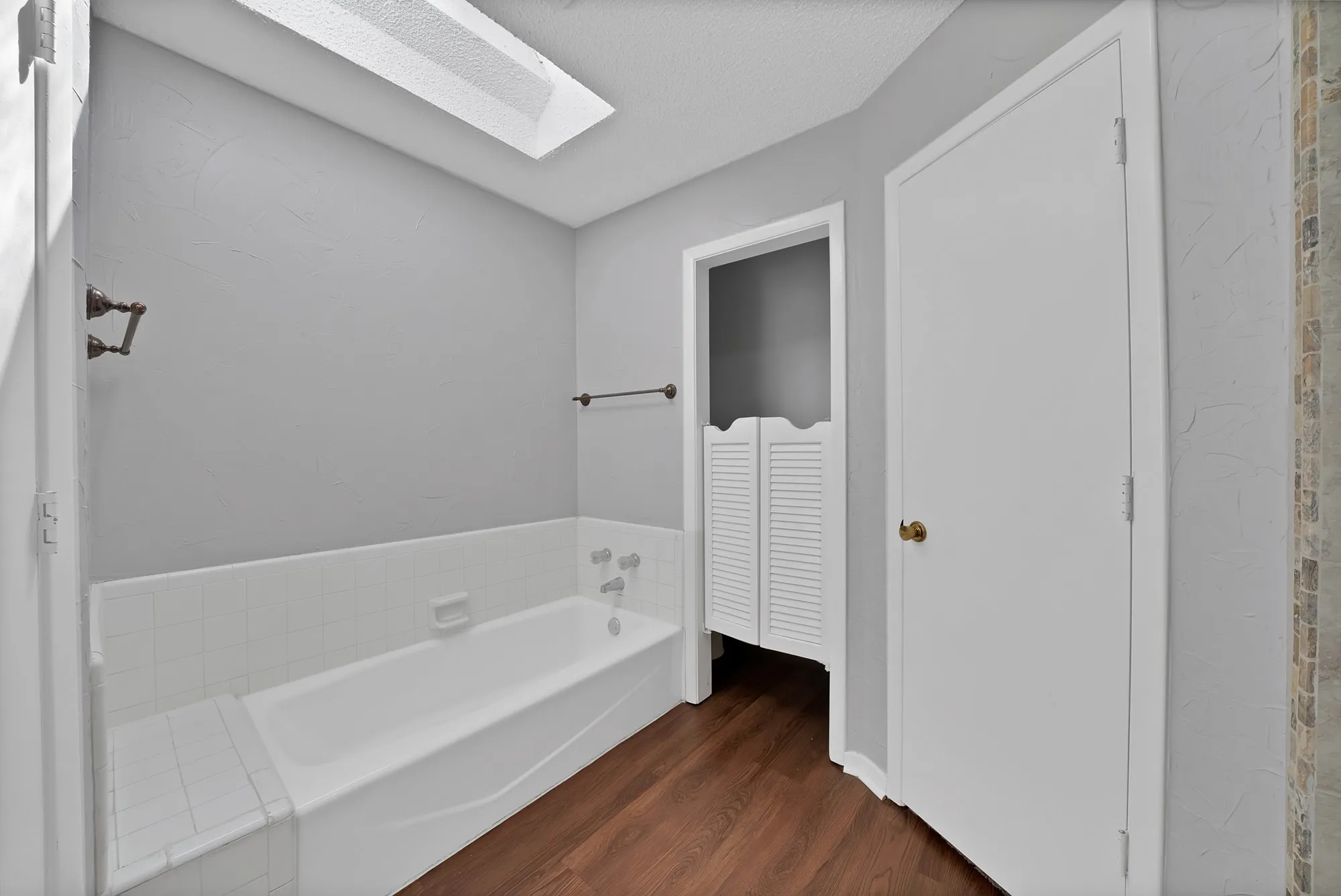 Full bath with dark wood-style floors, a garden tub, a skylight, and a closet