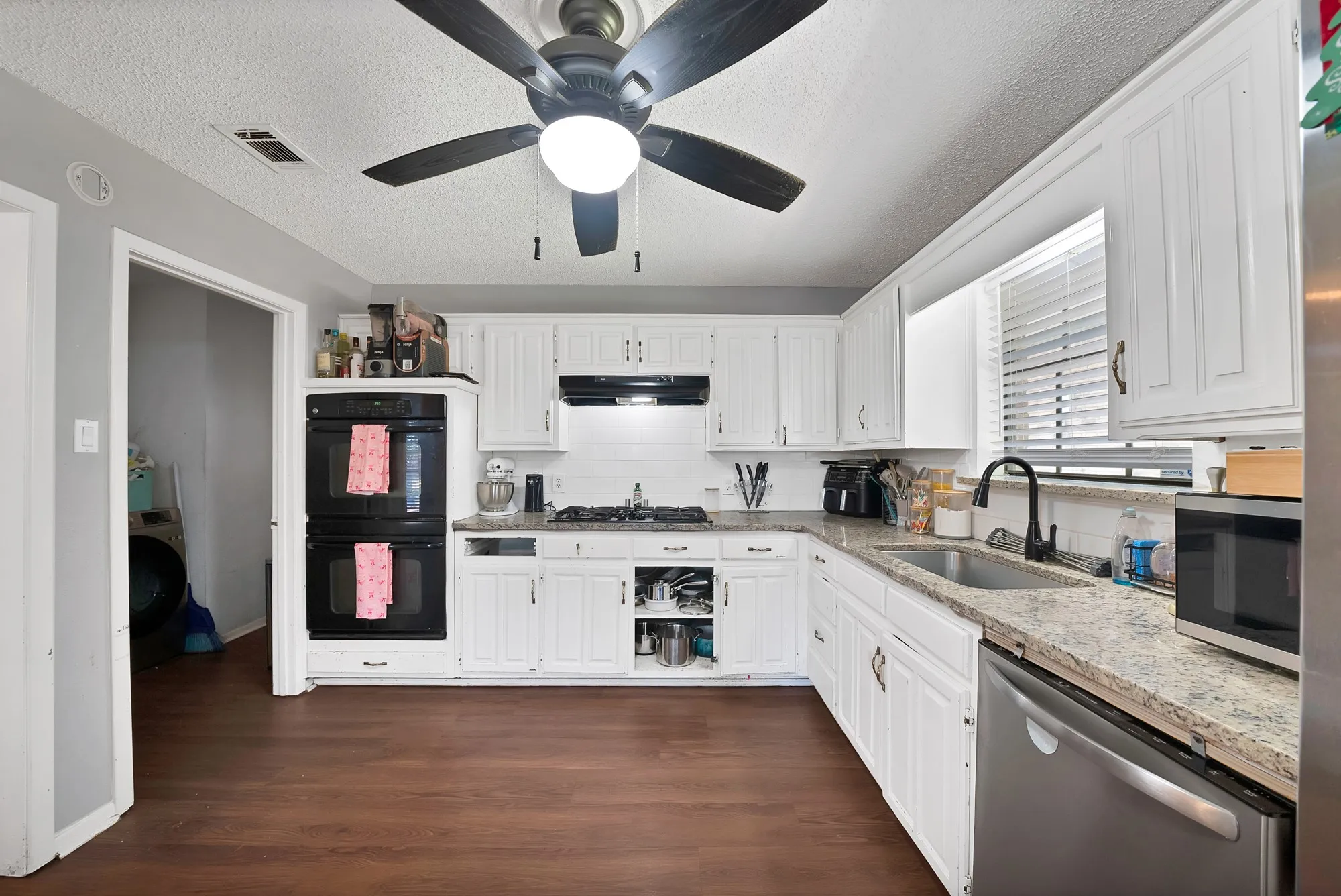 Kitchen with stainless steel appliances, a textured ceiling, white cabinets, light stone countertops, and backsplash