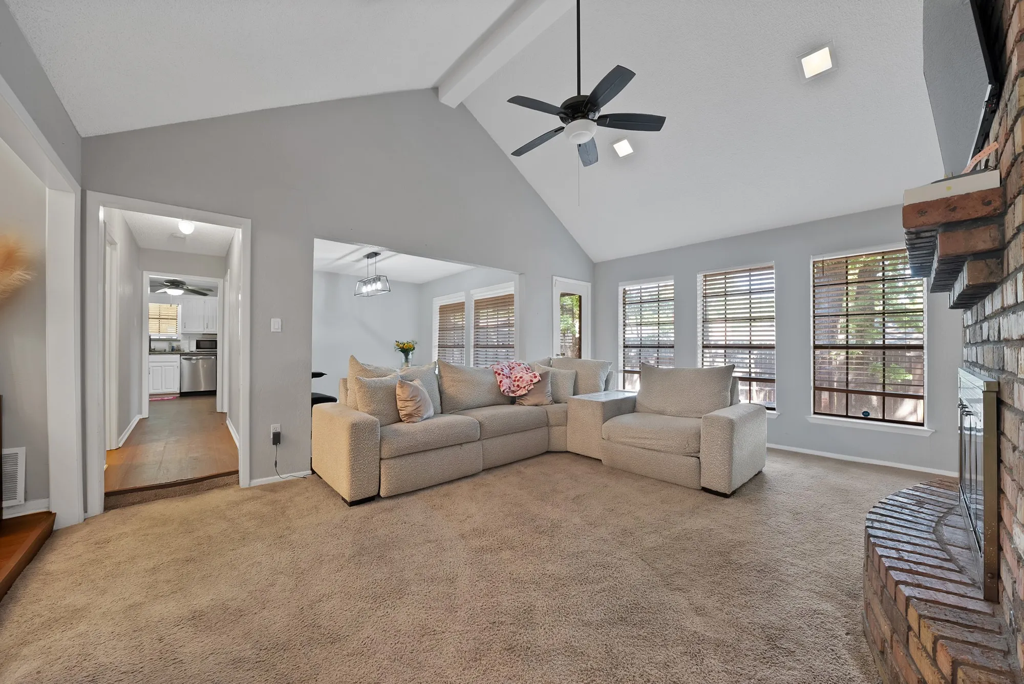 Carpeted living area with ceiling fan and a fireplace with raised hearth