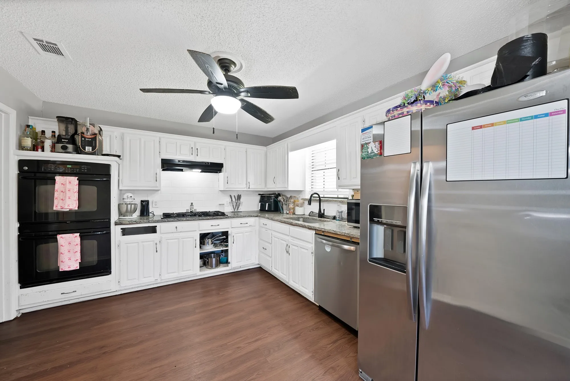 Kitchen featuring stainless steel appliances, a textured ceiling, white cabinets, dark wood-style flooring, and a ceiling fan