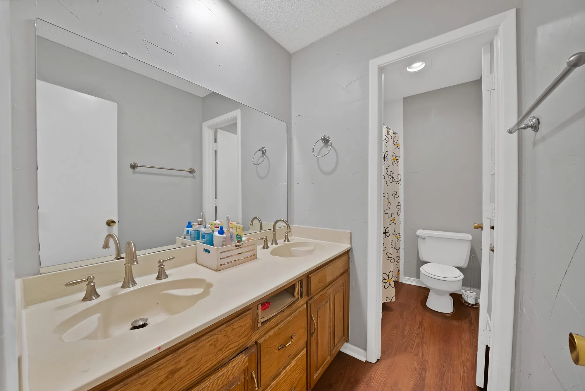 Full bath with a shower with shower curtain, double vanity, dark wood finished floors, and a textured ceiling