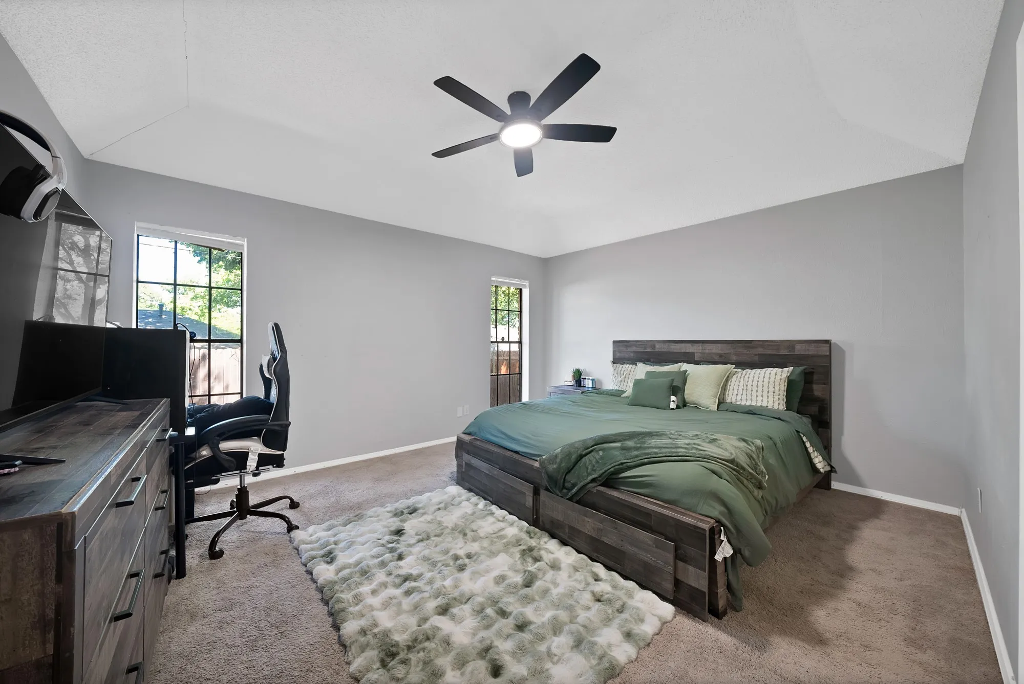 Carpeted bedroom featuring an office area, multiple windows, a ceiling fan, and lofted ceiling