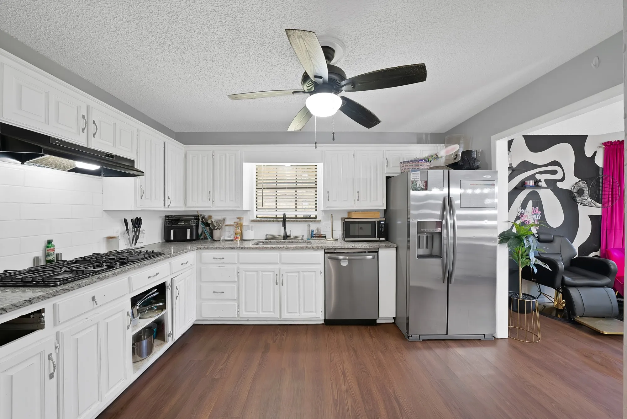 Kitchen with stainless steel appliances, light stone counters, dark wood-type flooring, white cabinetry, and a textured ceiling