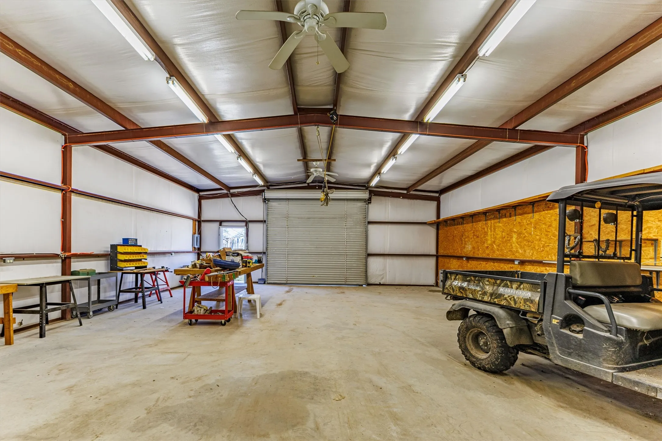 Spacious utility building with a large roll-up door, exposed metal beam construction, and concrete flooring