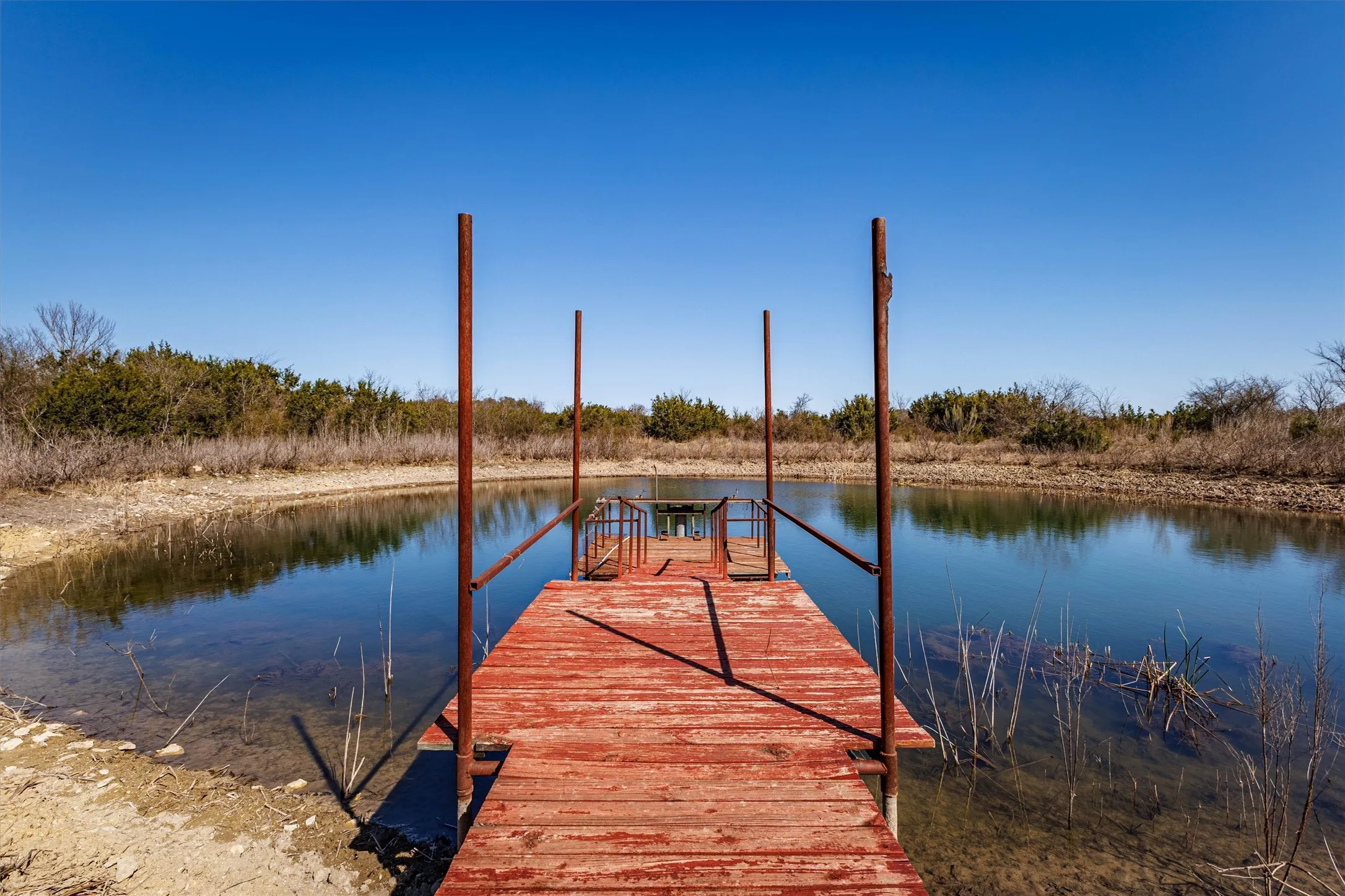 The property features a red wooden dock extending over a body of water, surrounded by natural vegetation