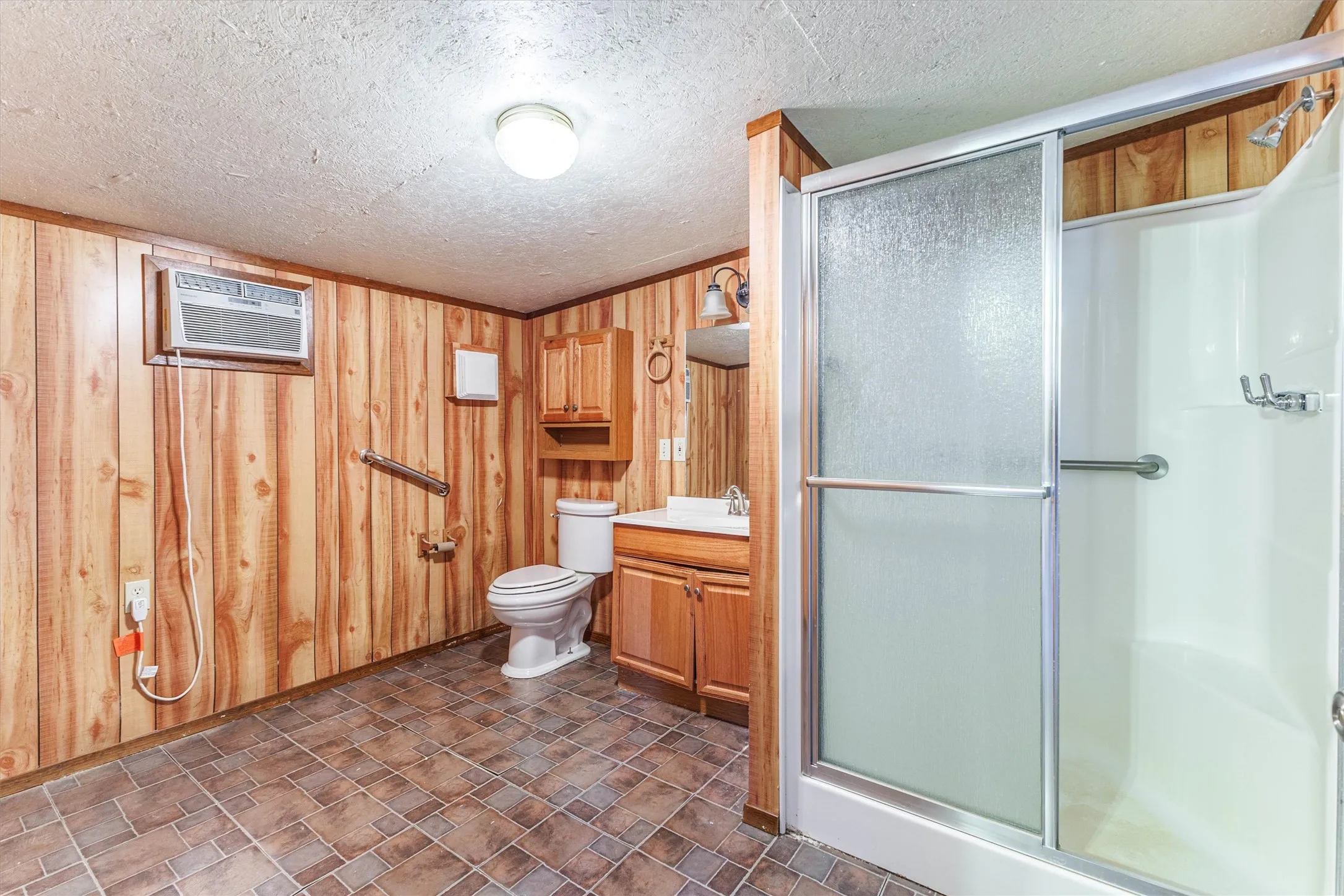 This bathroom features wood paneling, a shower with a sliding glass door, and a vanity with a sink and storage
