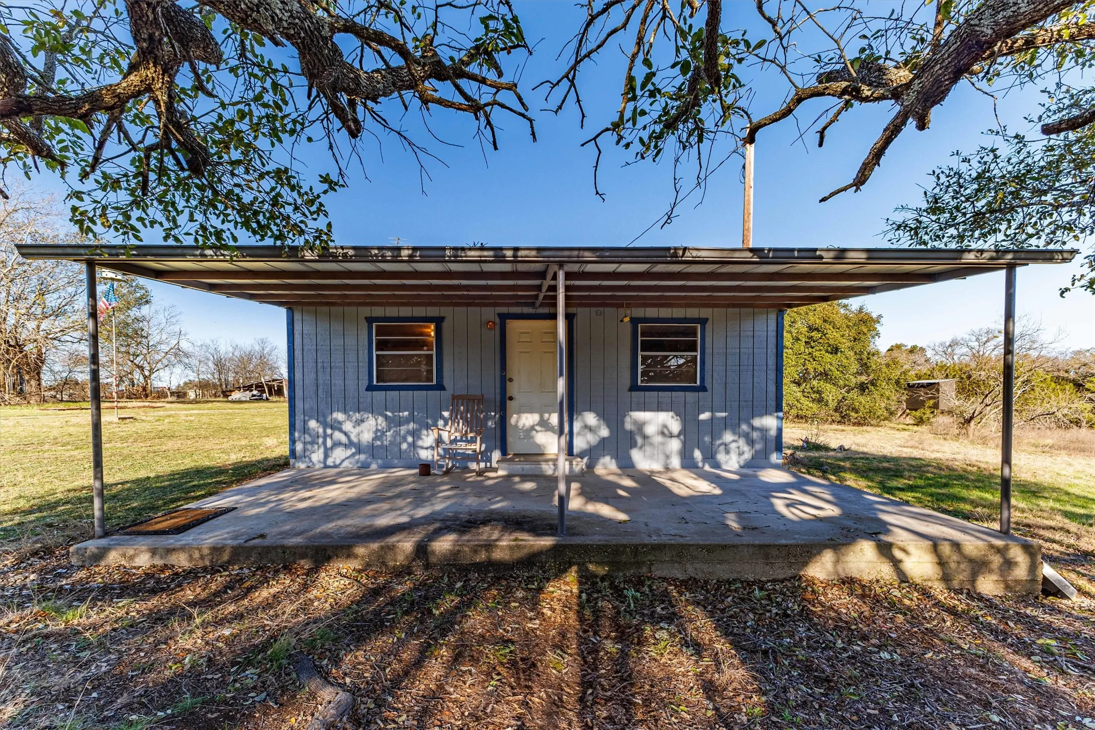 The property features a concrete porch with a metal roof extension, supported by metal posts