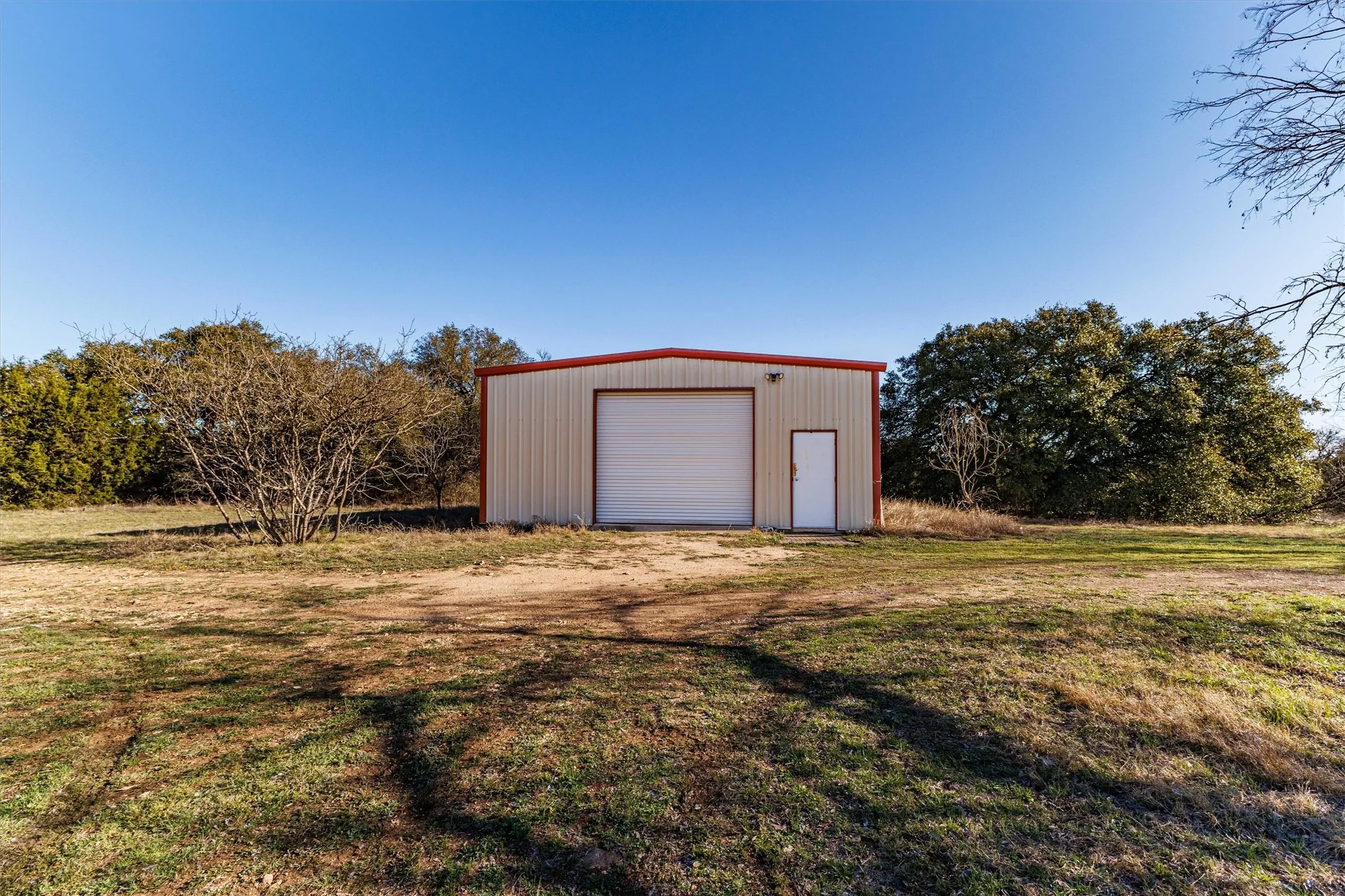 The property features a metal outbuilding with a roll-up door and a side entry door, surrounded by natural landscaping and trees