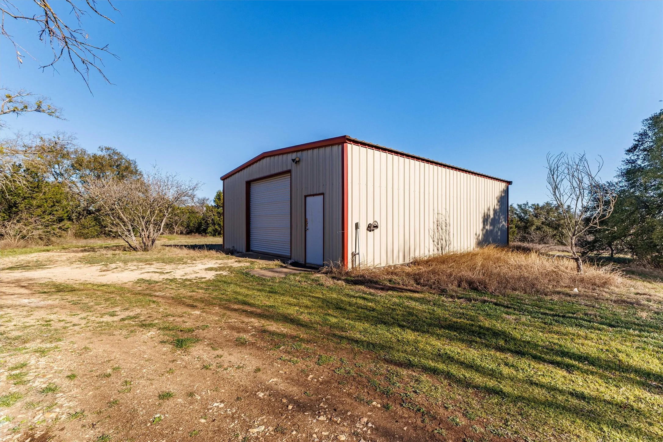 This property features a spacious metal building with a roll-up garage door and a separate entry door, set on a lot with both cleared and treed areas