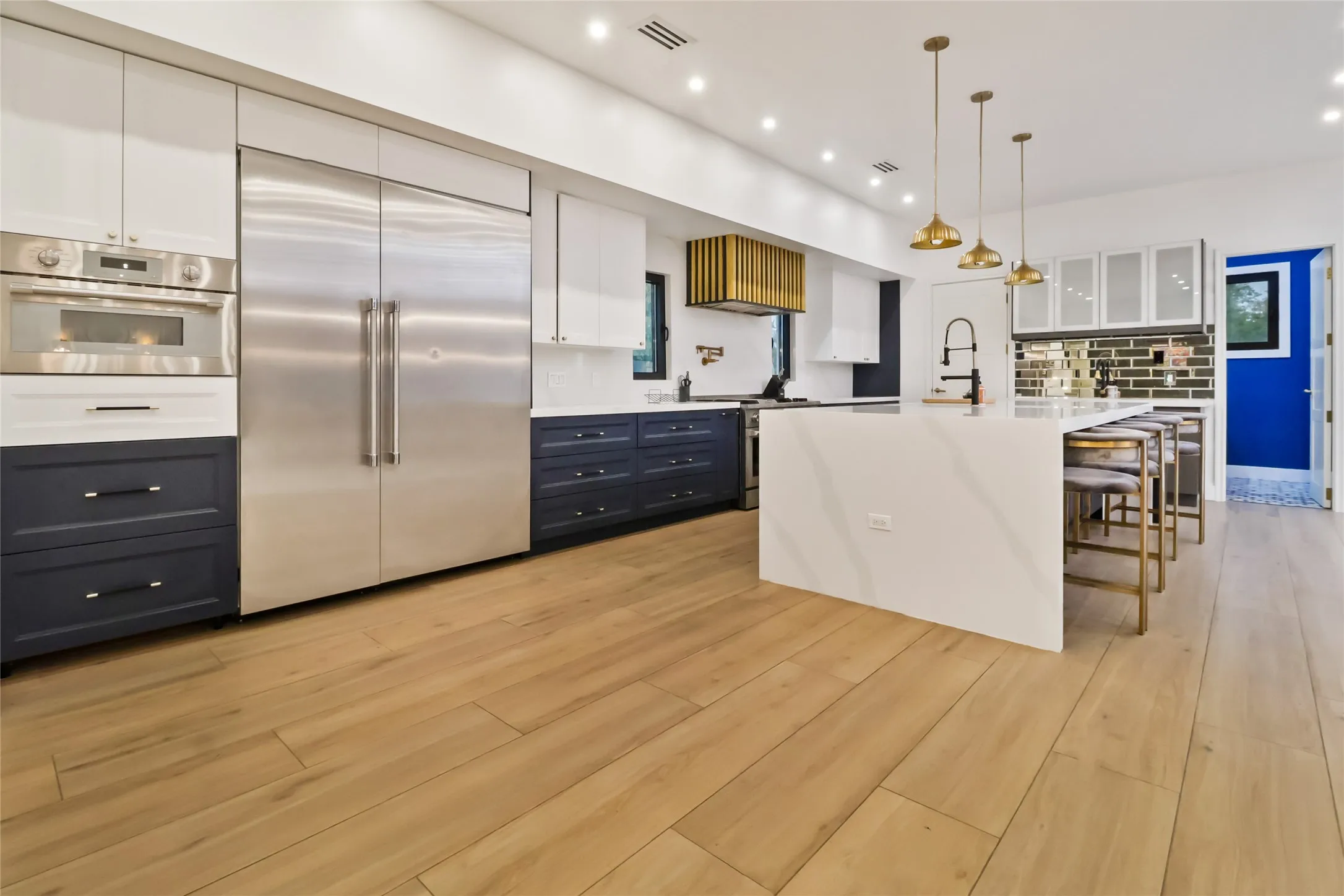 Kitchen with white cabinets, appliances with stainless steel finishes, a kitchen bar, decorative light fixtures, and light wood-style floors