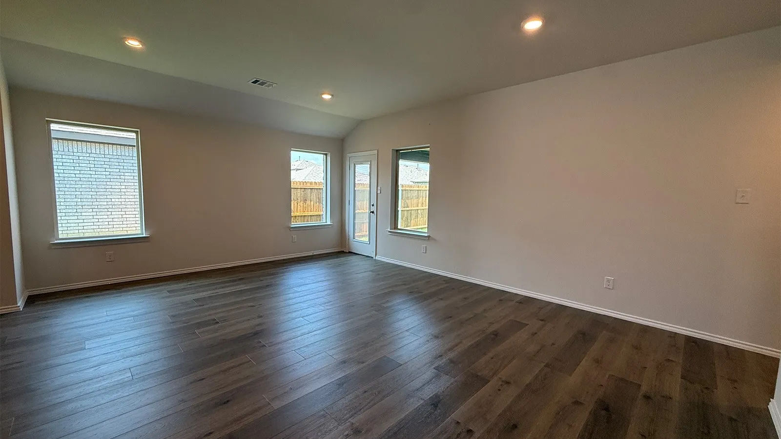Spacious interior featuring wood-finish flooring, recessed lighting, neutral wall tones, multiple windows, and a glass-paneled door