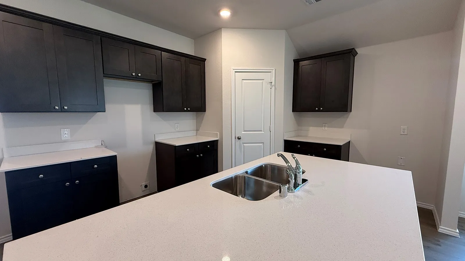 Kitchen island featuring a dual basin sink with chrome faucet, complemented by white countertops and dark wood cabinetry
