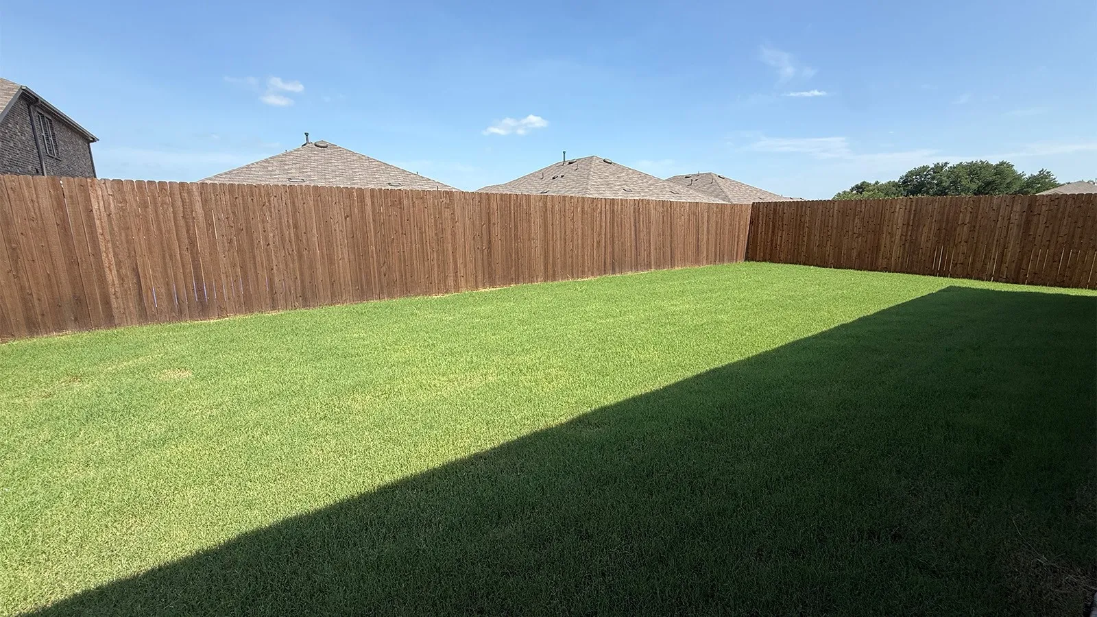 Expansive backyard featuring a natural wood privacy fence, substantial green lawn, and clear sky