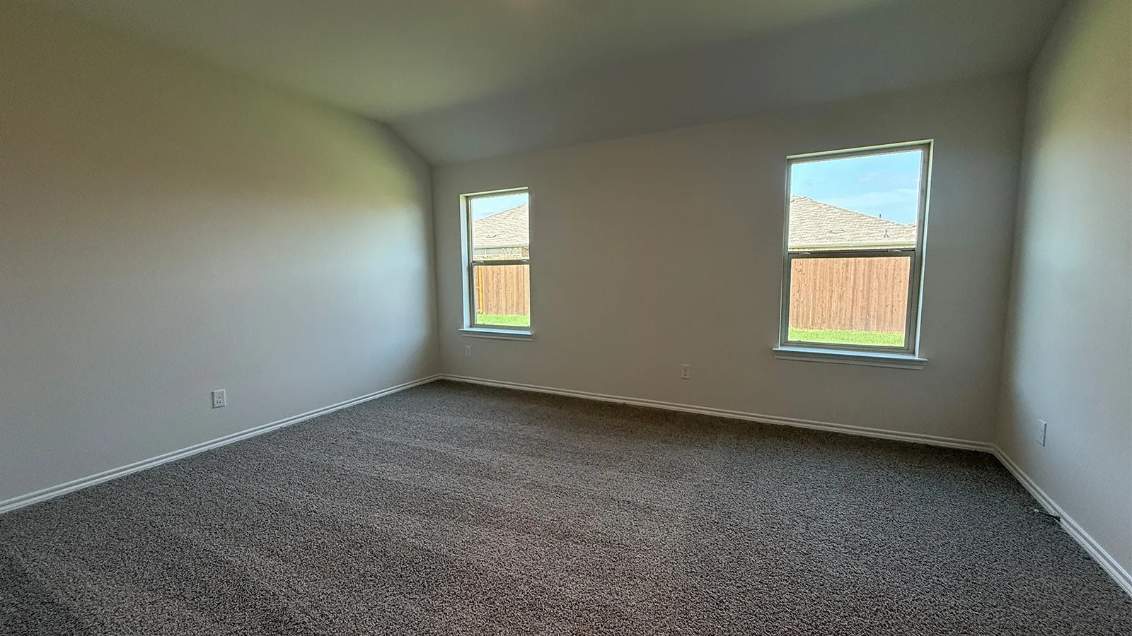 Carpeted room featuring two double-hung windows with white trim, light neutral wall finishes, and a vaulted ceiling