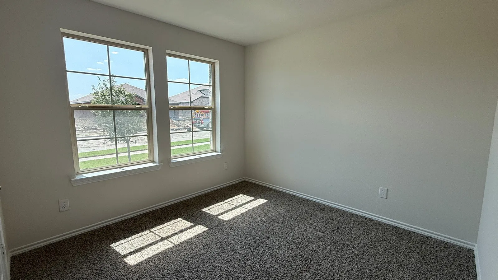 Bright room featuring two large windows, neutral wall tones, textured carpeting, and white trim