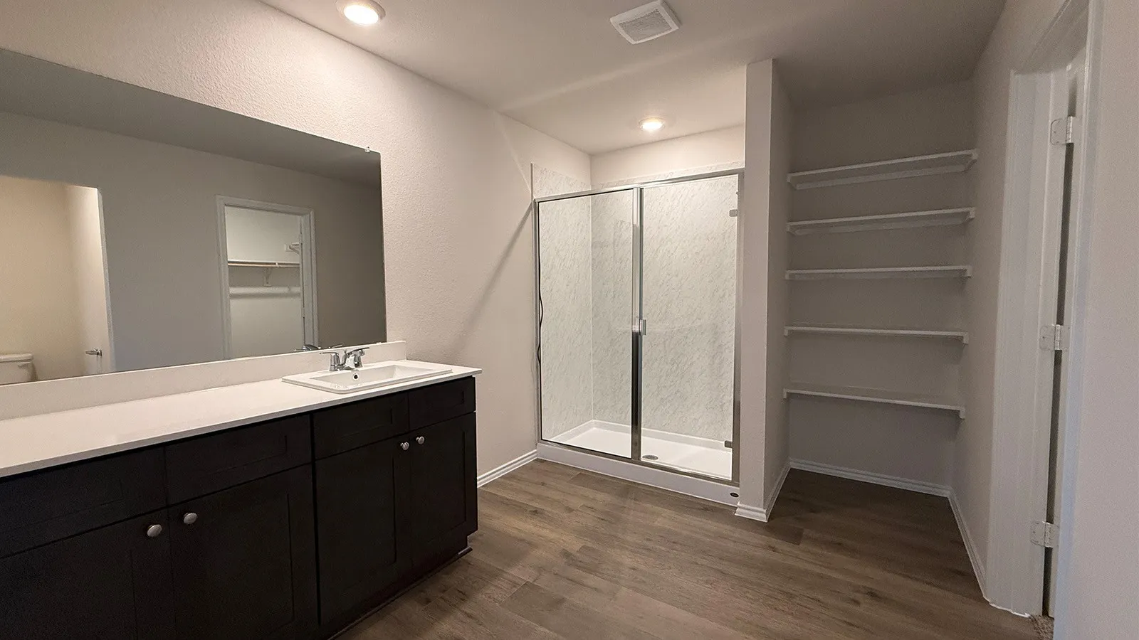 Bathroom featuring a dark wood-finish vanity with a single sink and white countertop, a glass-enclosed shower, and wood-finish flooring