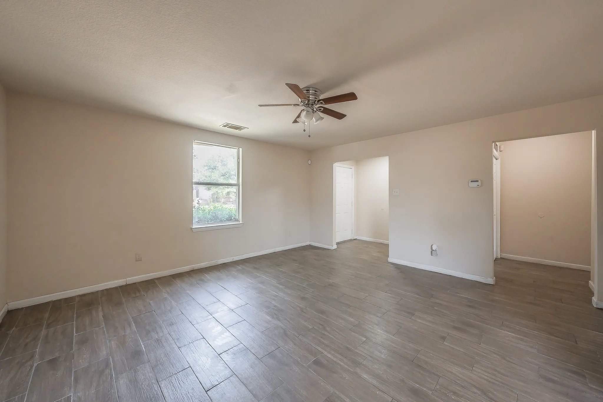Spacious room featuring wood-finish tile flooring, neutral wall tones, and a ceiling fan with integrated lighting
