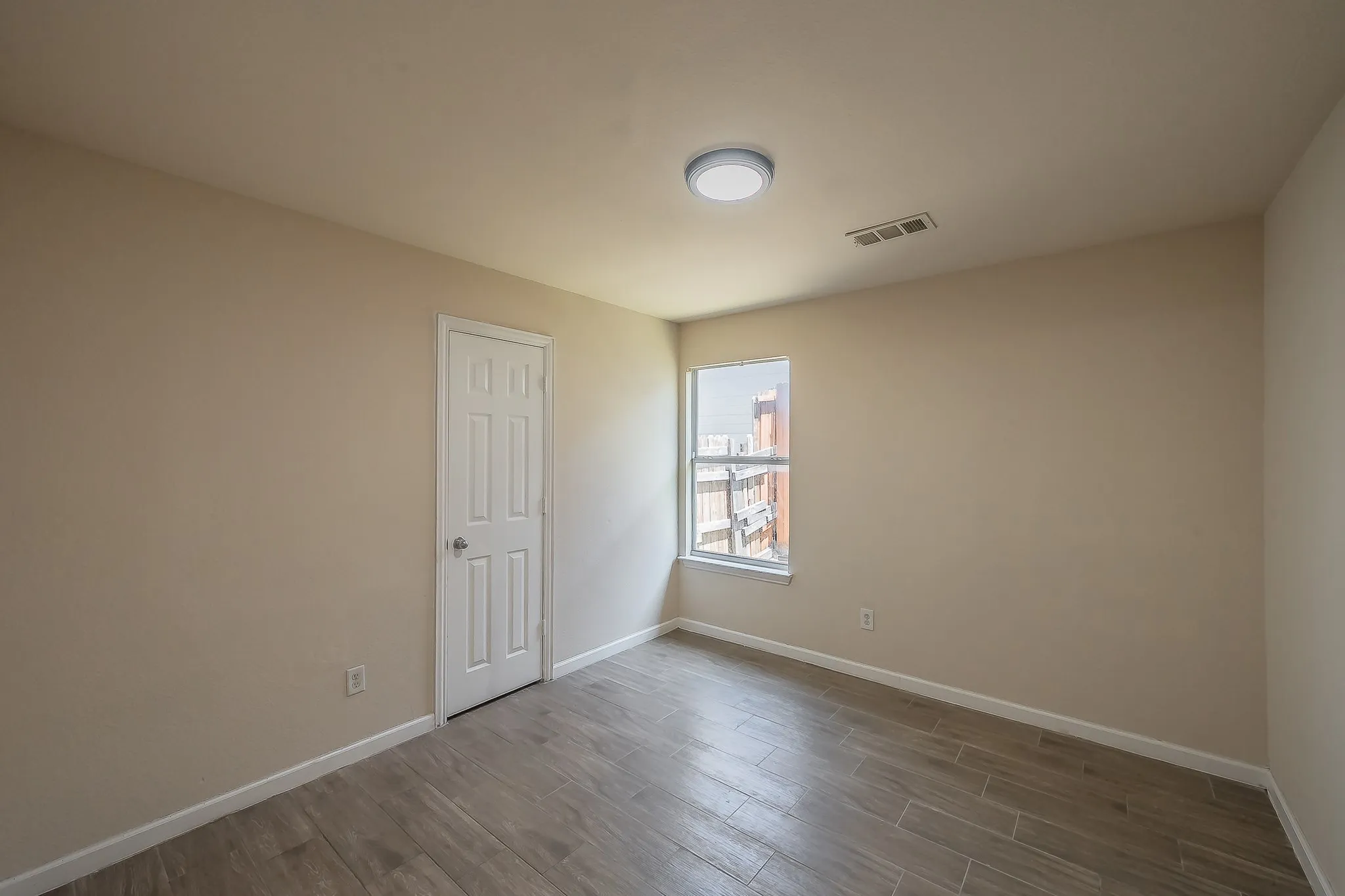 Neutral-toned room with wood-finish tile flooring, a white paneled door, and a single window with white trim