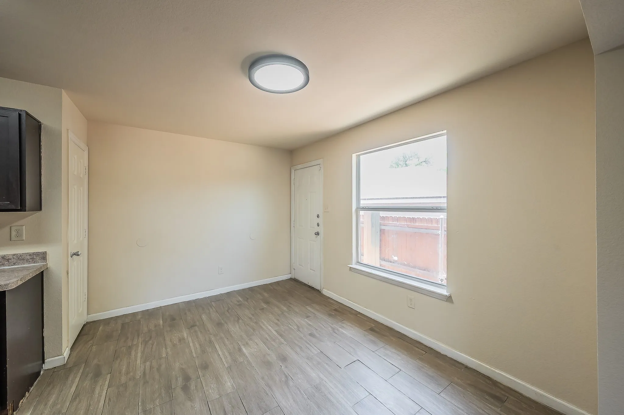 Open-concept room featuring wood-finish flooring, a contemporary flush-mount ceiling light, and a window with a white frame