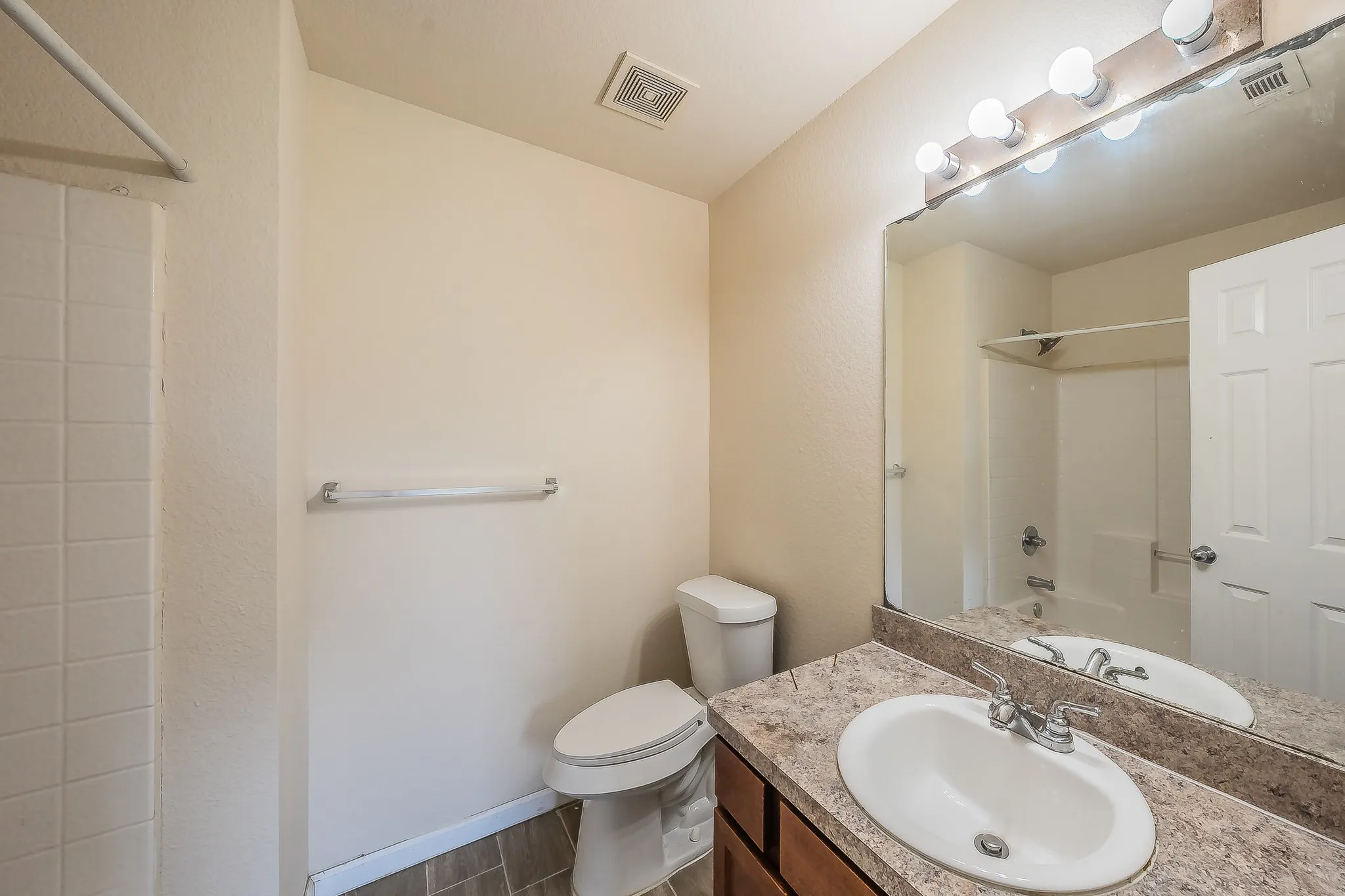 Bathroom featuring a vanity with an oval sink and a textured countertop, a mounted mirror with overhead lighting, wood-finish flooring, a toilet, and a tiled shower/tub combination