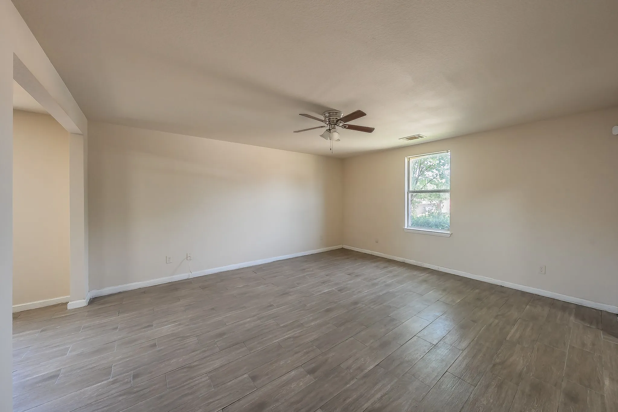 Spacious room featuring wood-finish flooring, neutral-toned walls, a ceiling fan, and natural light from a double-pane window