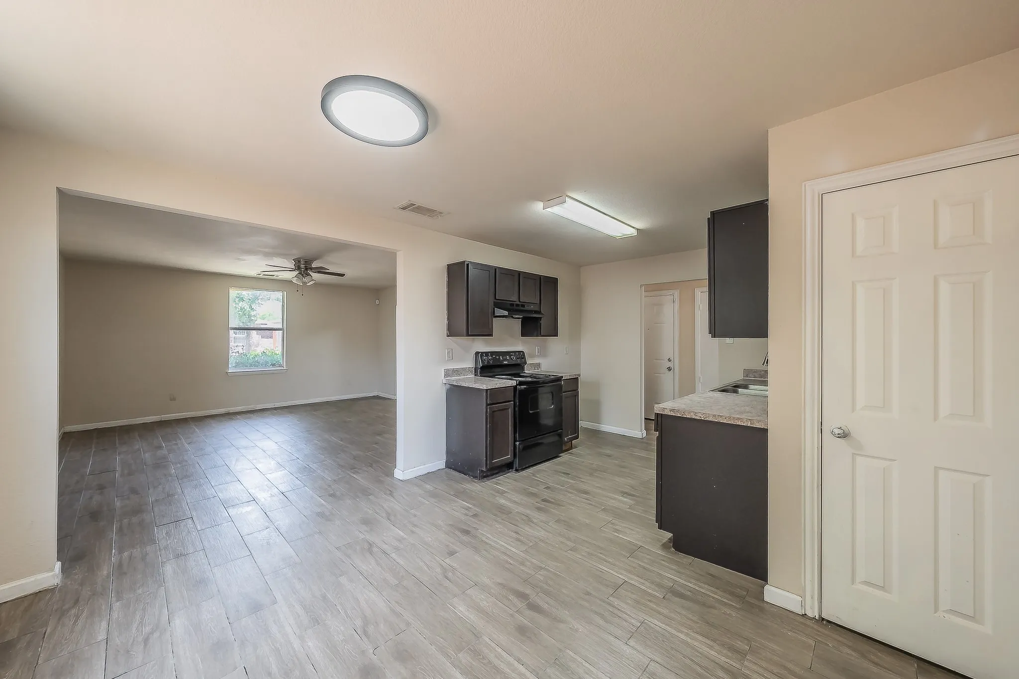 Kitchen and living area featuring wood-finish tile flooring, dark wood cabinetry, light-toned countertops, and a black appliance suite including a range