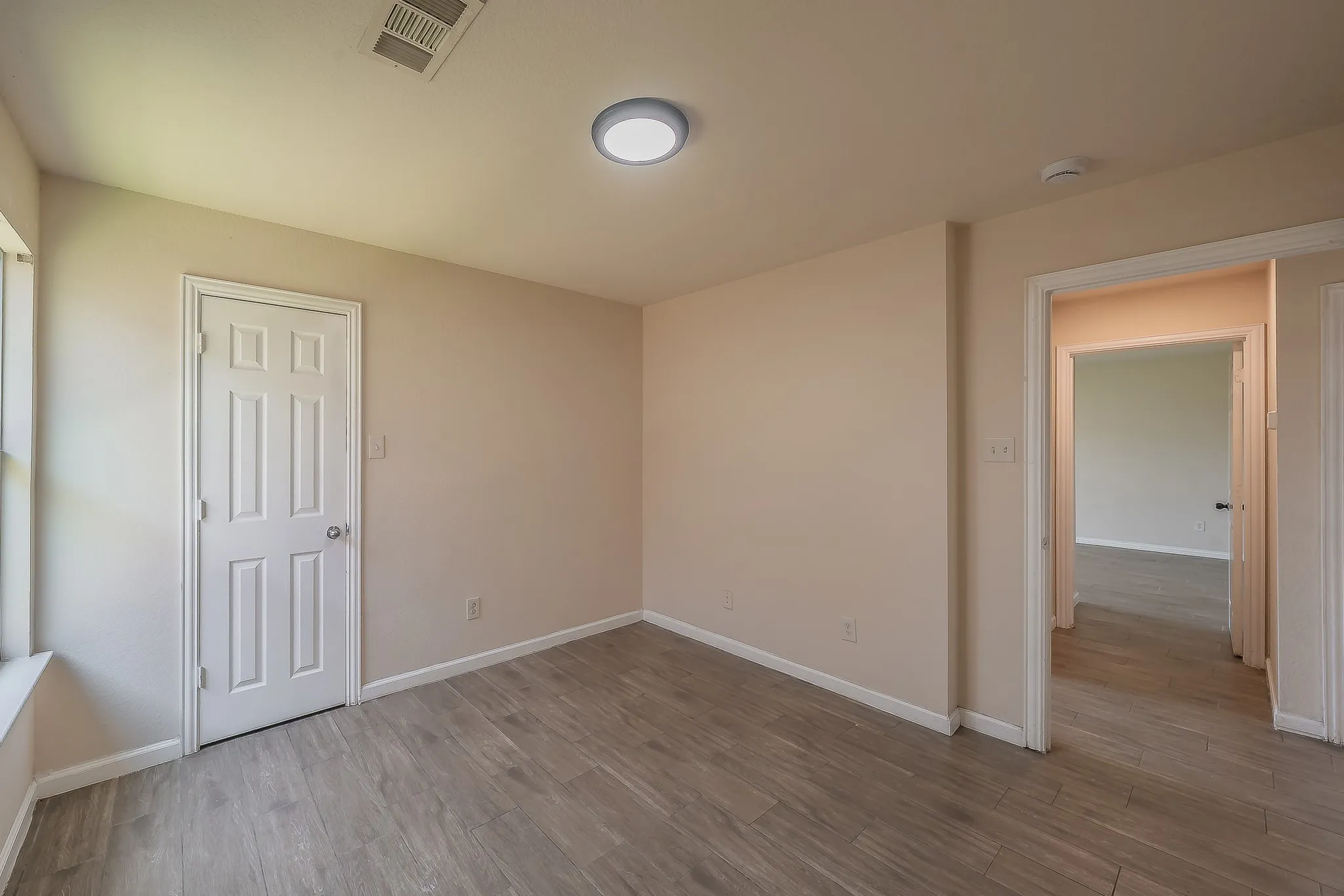 Room featuring wood-finish flooring, a six-panel interior door, and a flush mount ceiling light fixture
