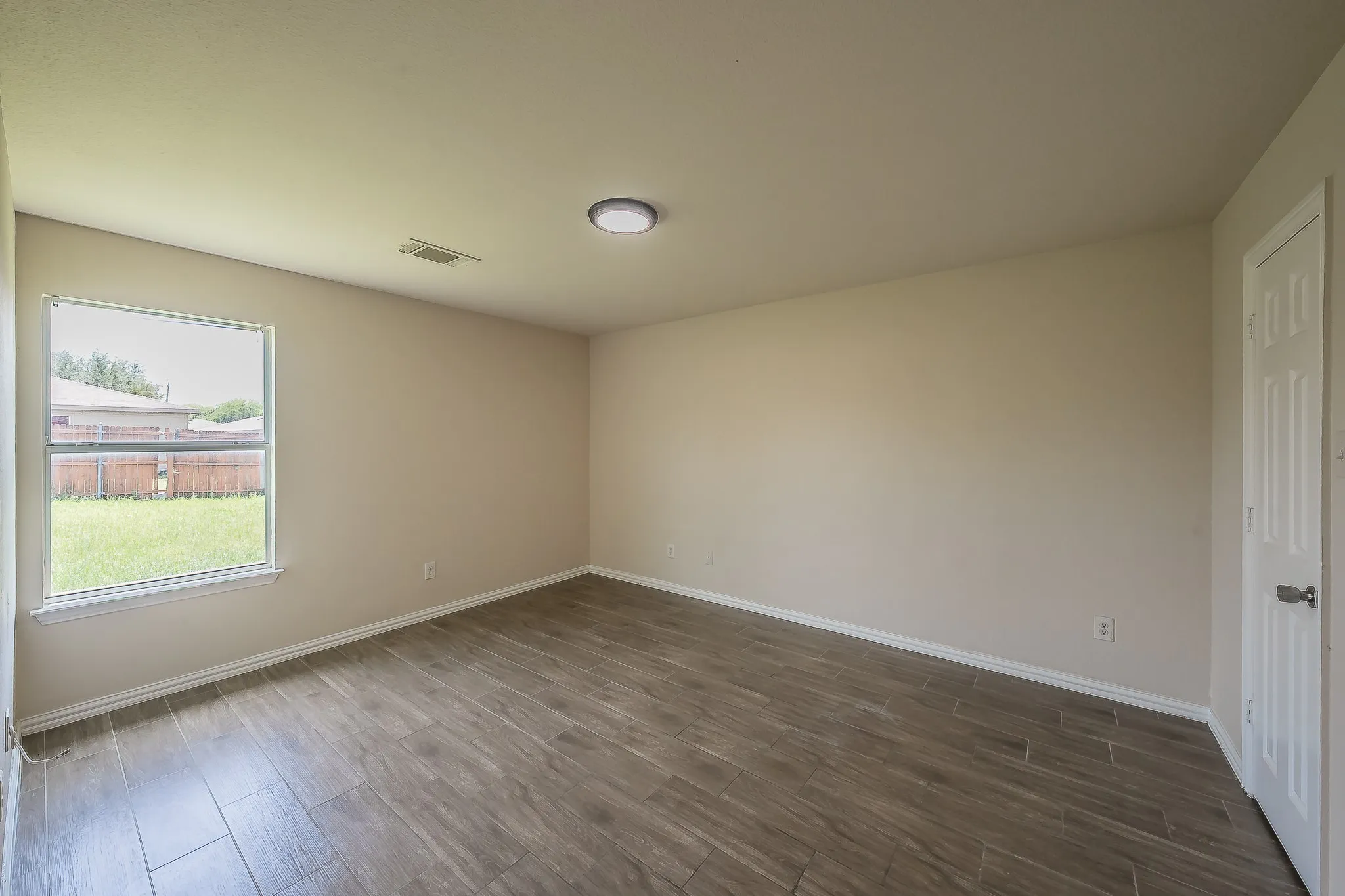 Spacious room featuring wood-finish tile flooring, neutral wall paint, a single window, and a white paneled door