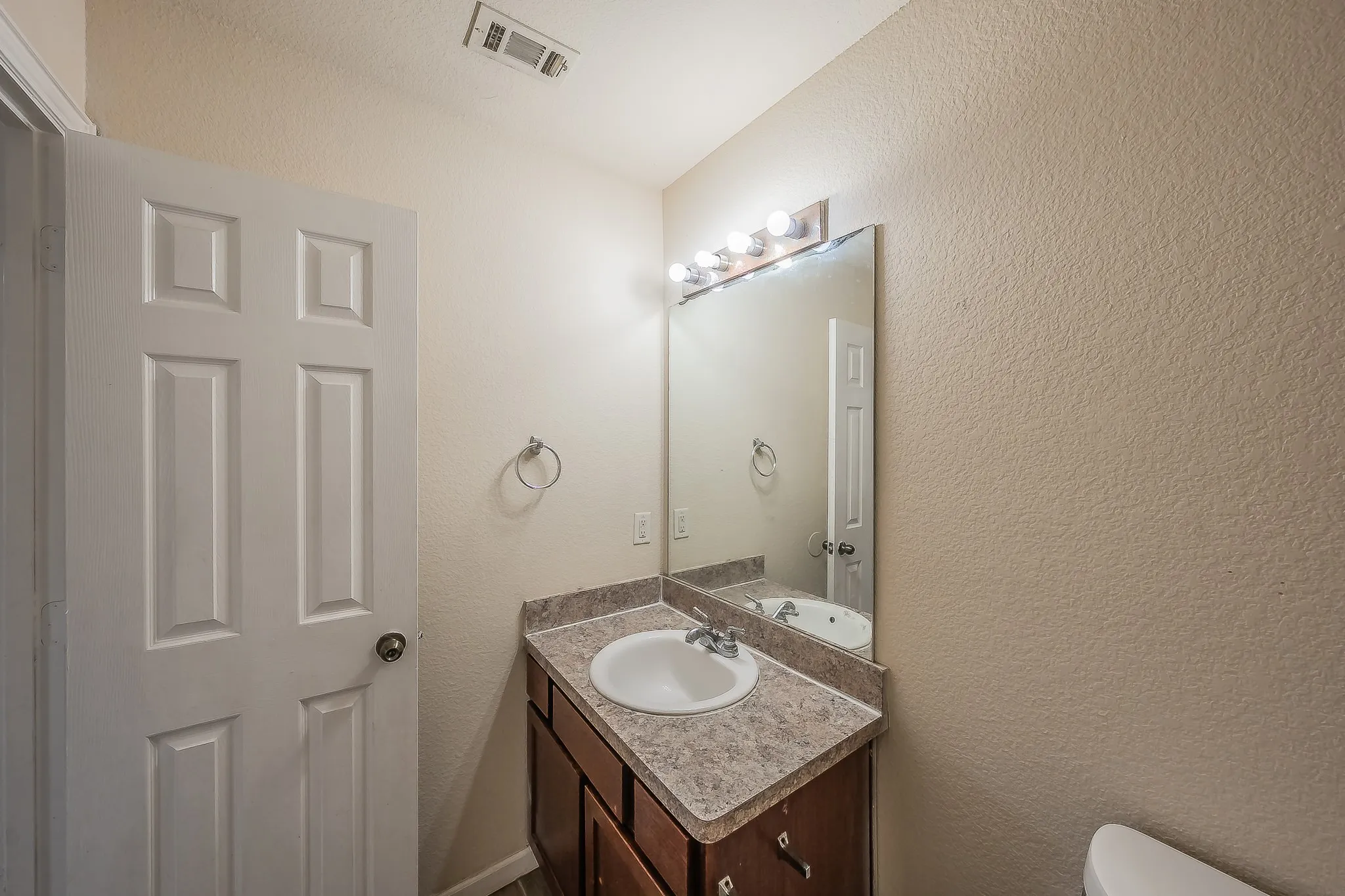 Bathroom featuring a single vanity with an integrated sink, brown cabinetry, and a speckled countertop