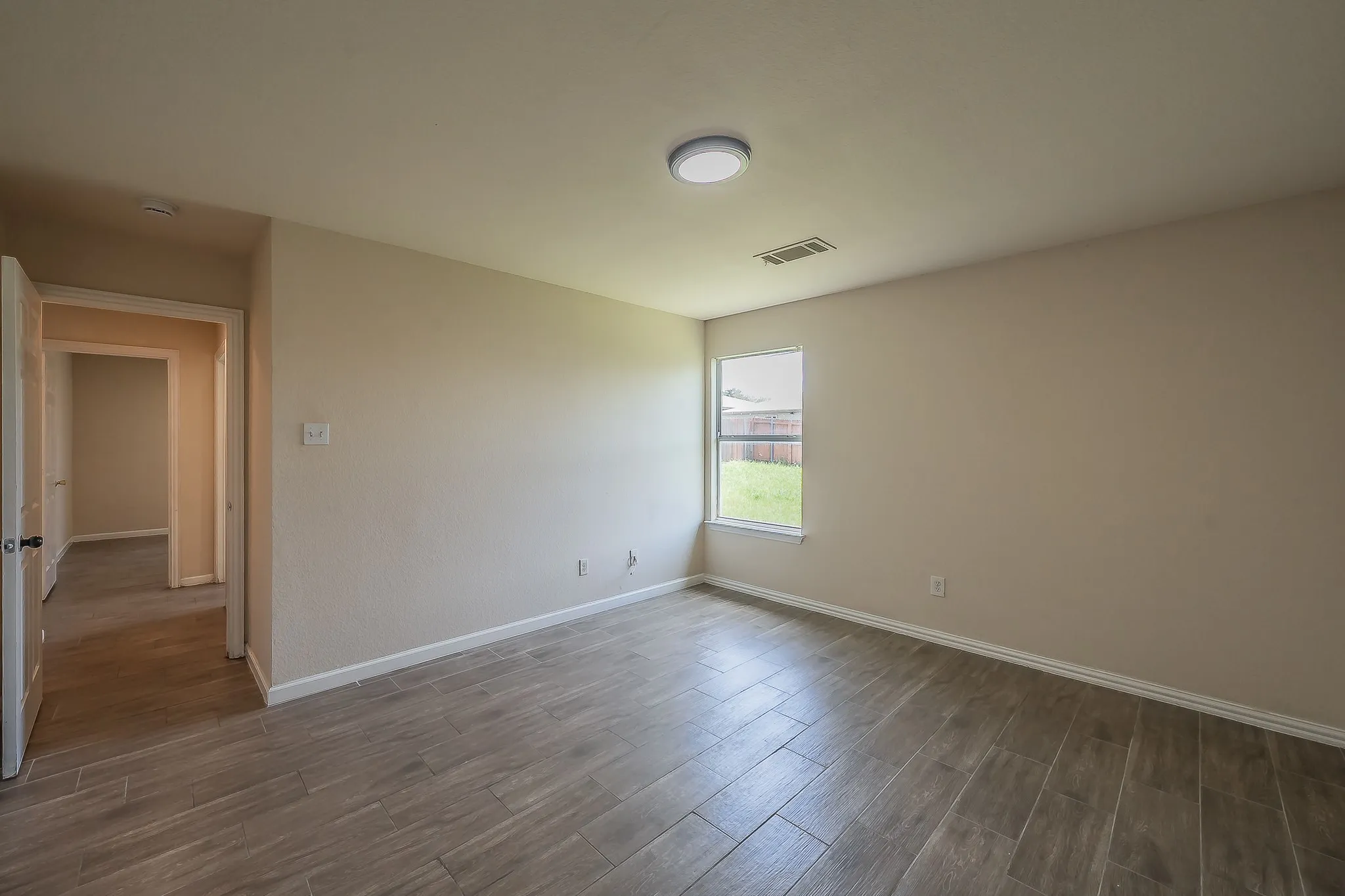 Neutral tone walls with white trim, wood-finish tile flooring, and a single window offering exterior light