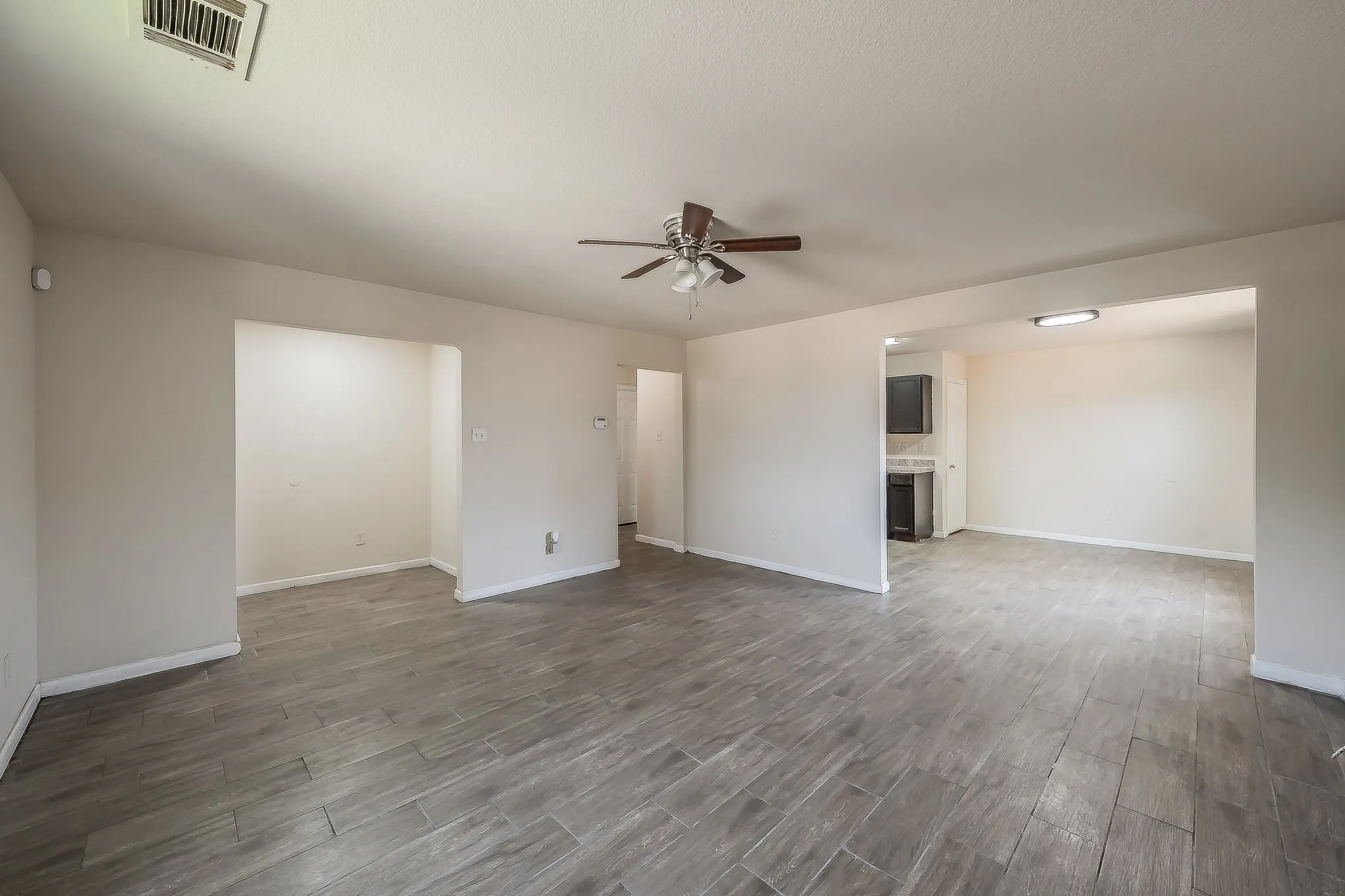 Spacious interior featuring wood-finish flooring, light neutral wall tones, and a ceiling fan with integrated lighting