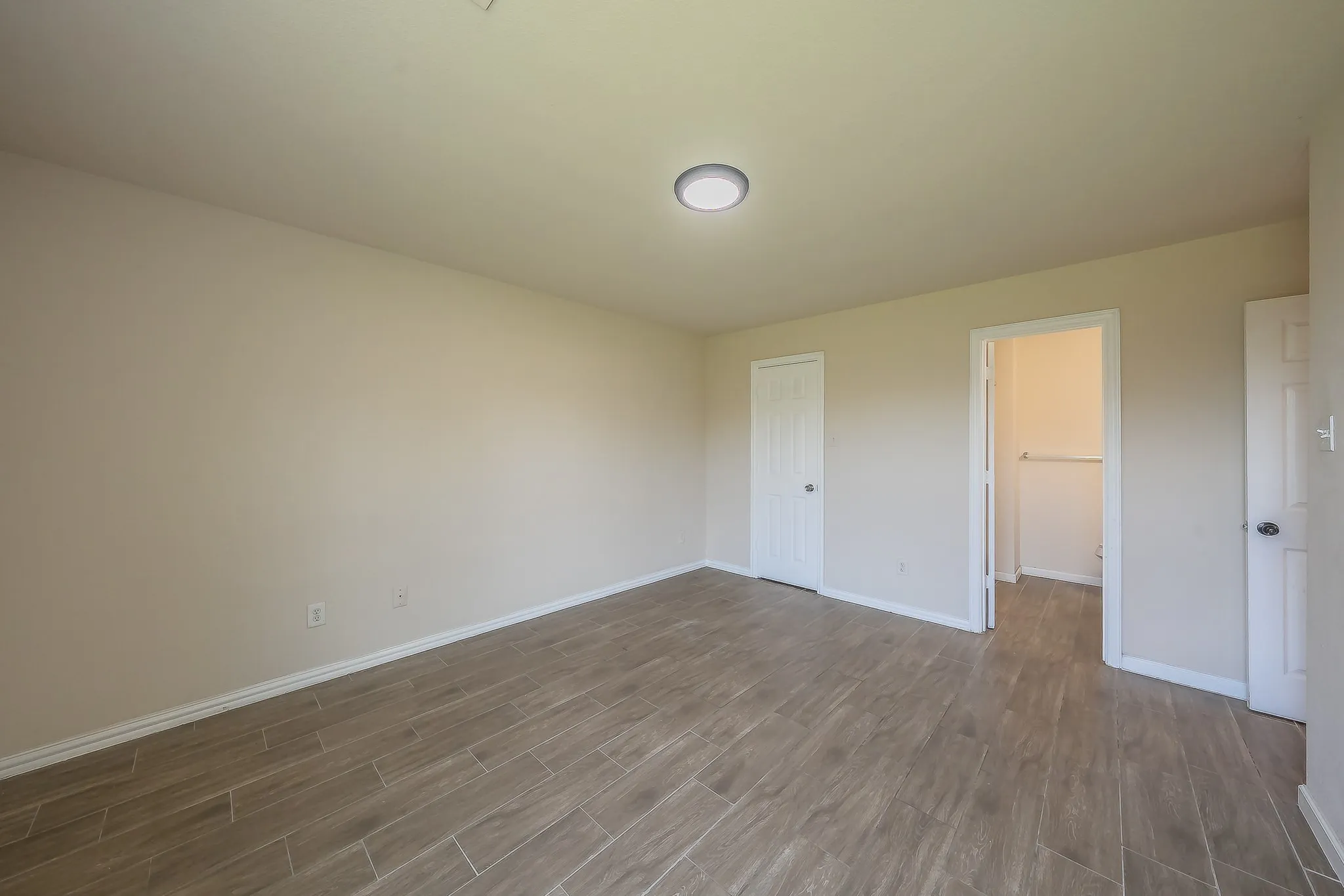 Spacious room featuring wood-finish tile flooring, recessed lighting, neutral wall tones, and white trim