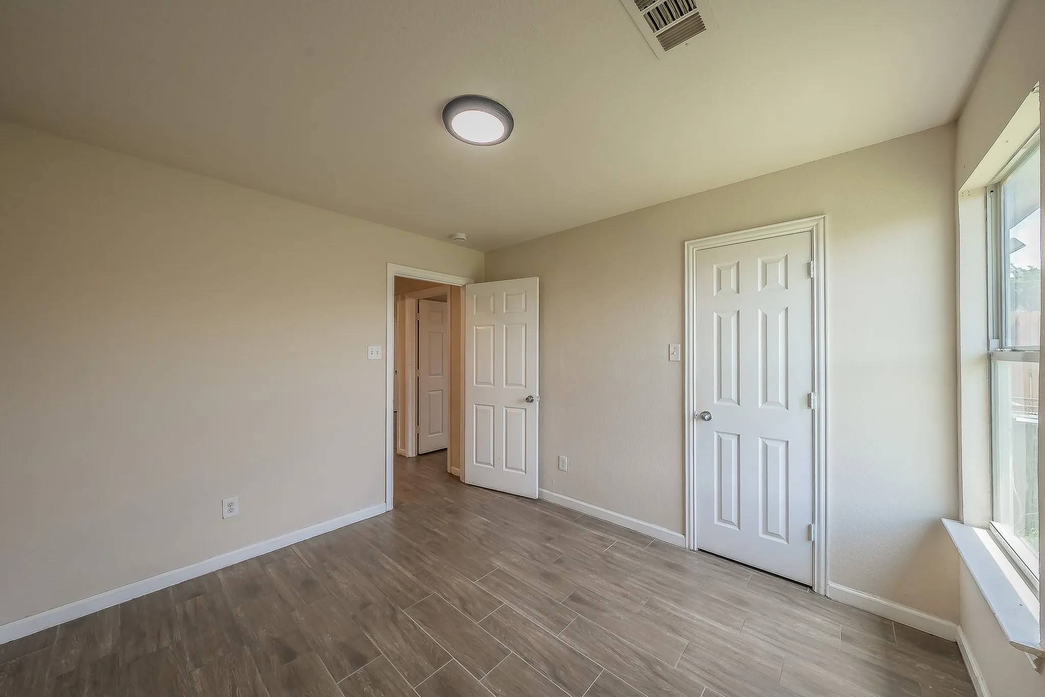 Spacious interior room featuring wood-look tile flooring, light-toned walls, white trim, and a contemporary flush-mount ceiling light