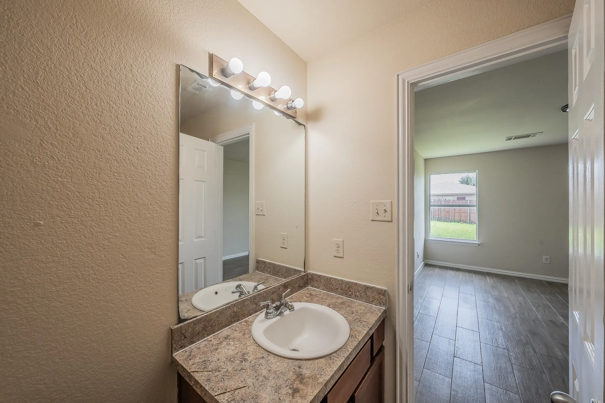 Bathroom vanity featuring a drop-in sink, dual-handle faucet, and a large mirror with a vanity light bar