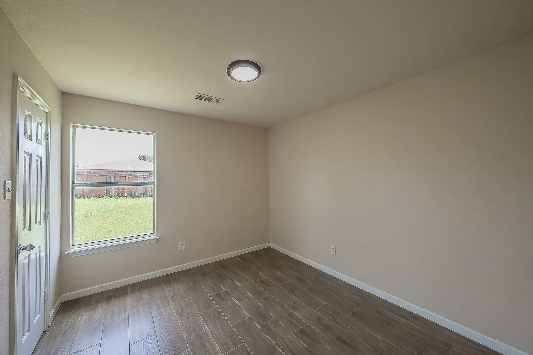 Interior room featuring wood-finish tile flooring, a window with exterior yard visibility, and a contemporary flush-mount ceiling light fixture