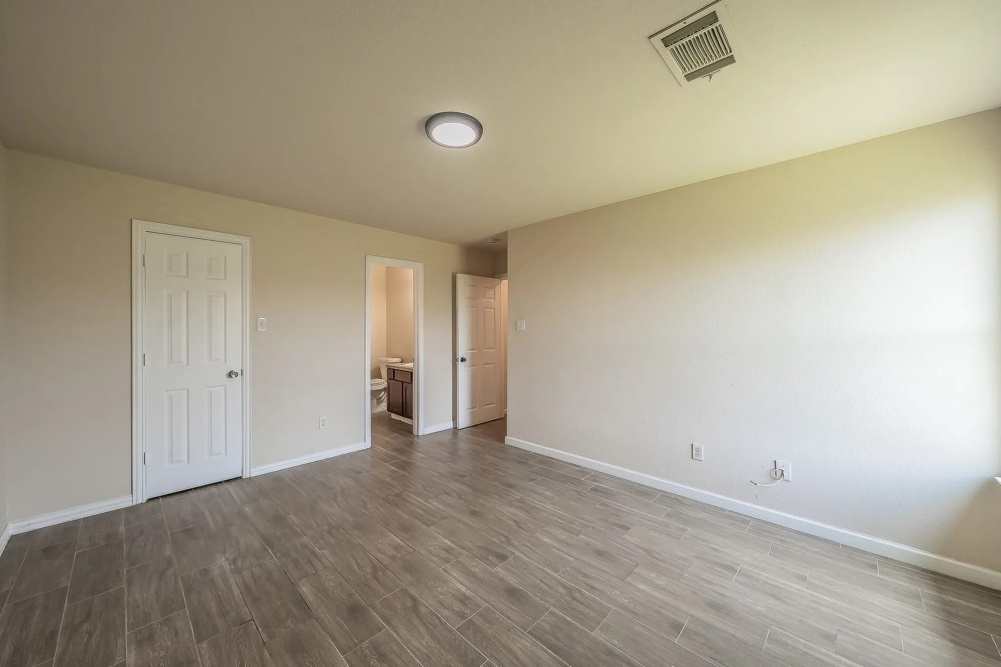 Spacious room with wood-finish tile flooring, neutral wall tones, white baseboards, and a contemporary flush-mount ceiling light