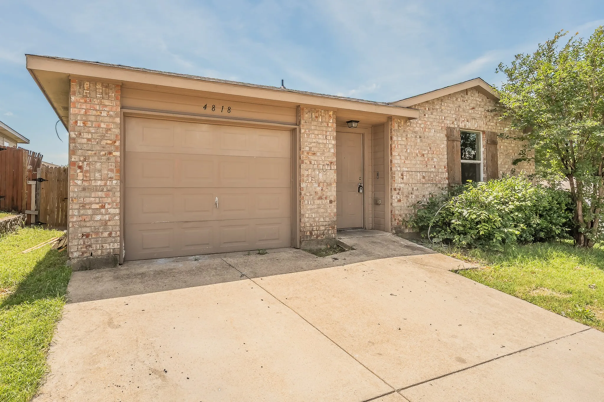 Brick veneer exterior featuring a single-car garage with a tan garage door, a concrete driveway, and a front entry door with an overhead light fixture