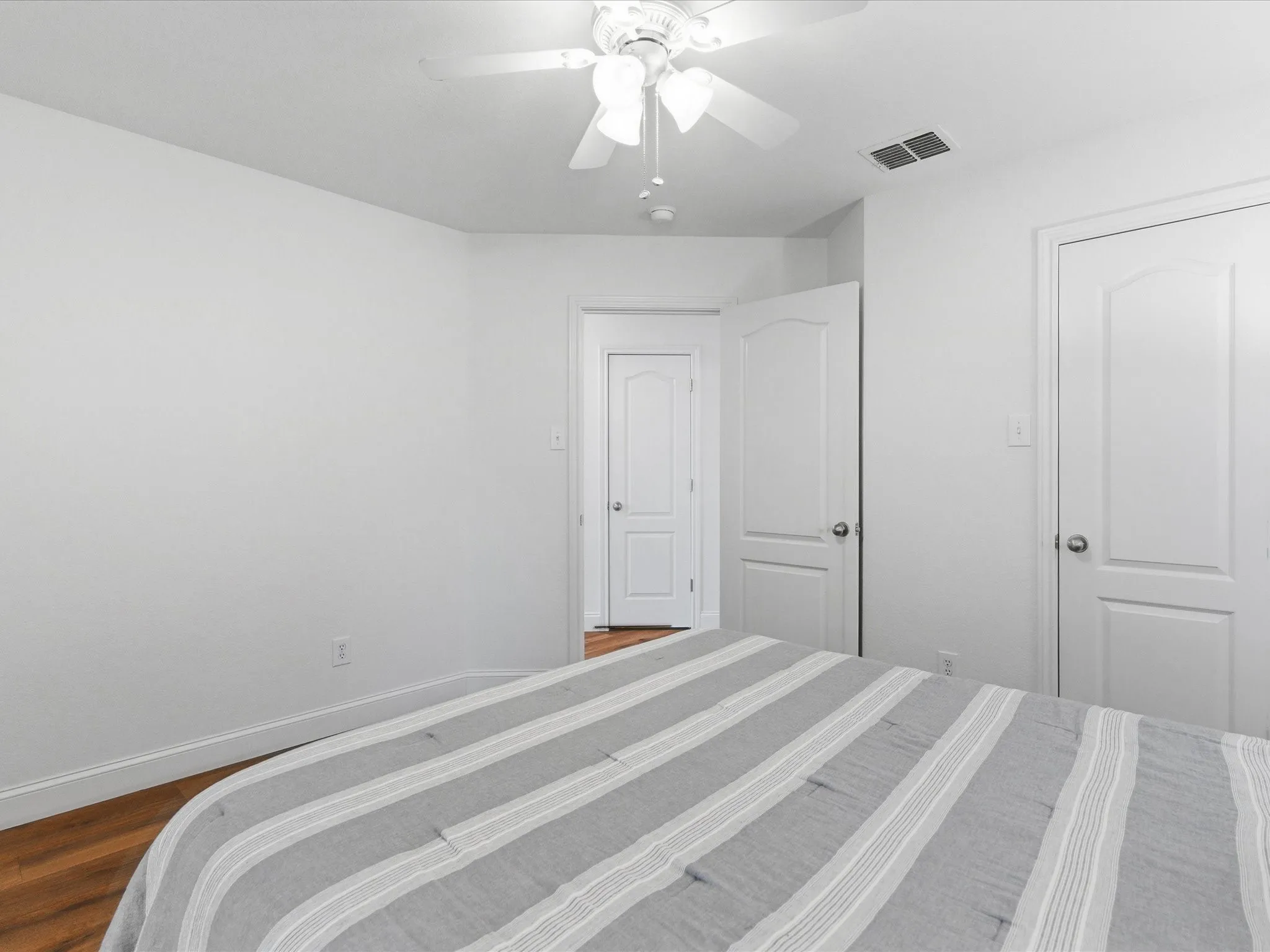 This room features hardwood flooring, white walls, and a ceiling fan with integrated lighting