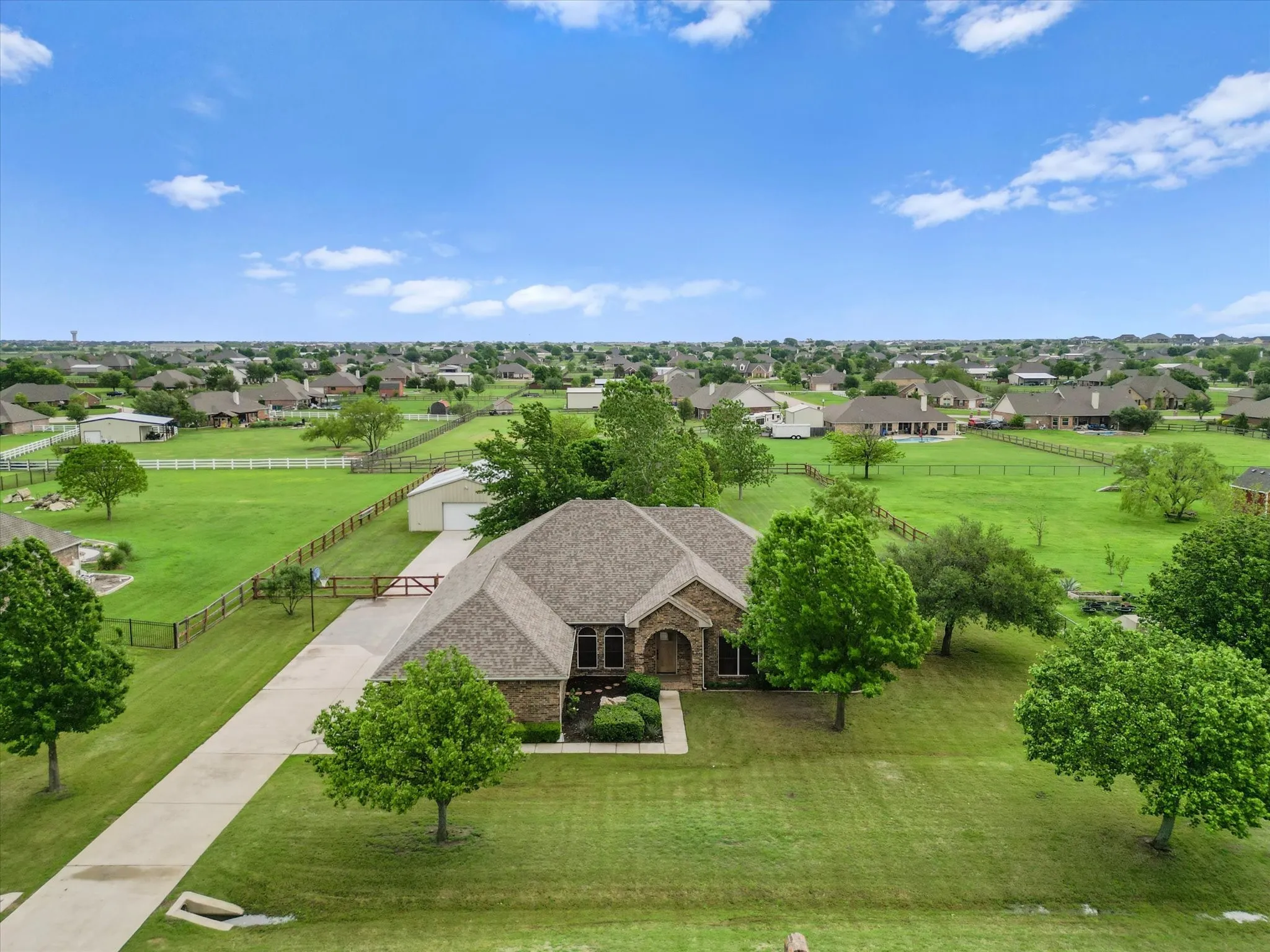 The property features an extensive green lawn, mature trees, and a long driveway leading to the house